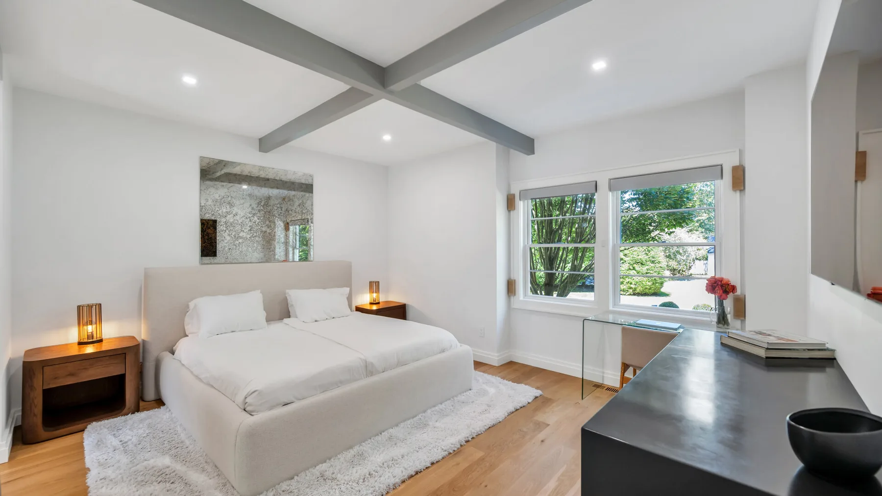 A bright bedroom with a bed, bedside tables, and large windows.
