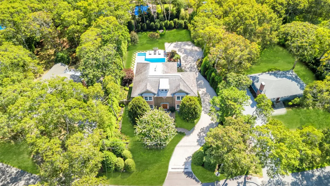 An aerial view of a house surrounded by trees and green lawn.