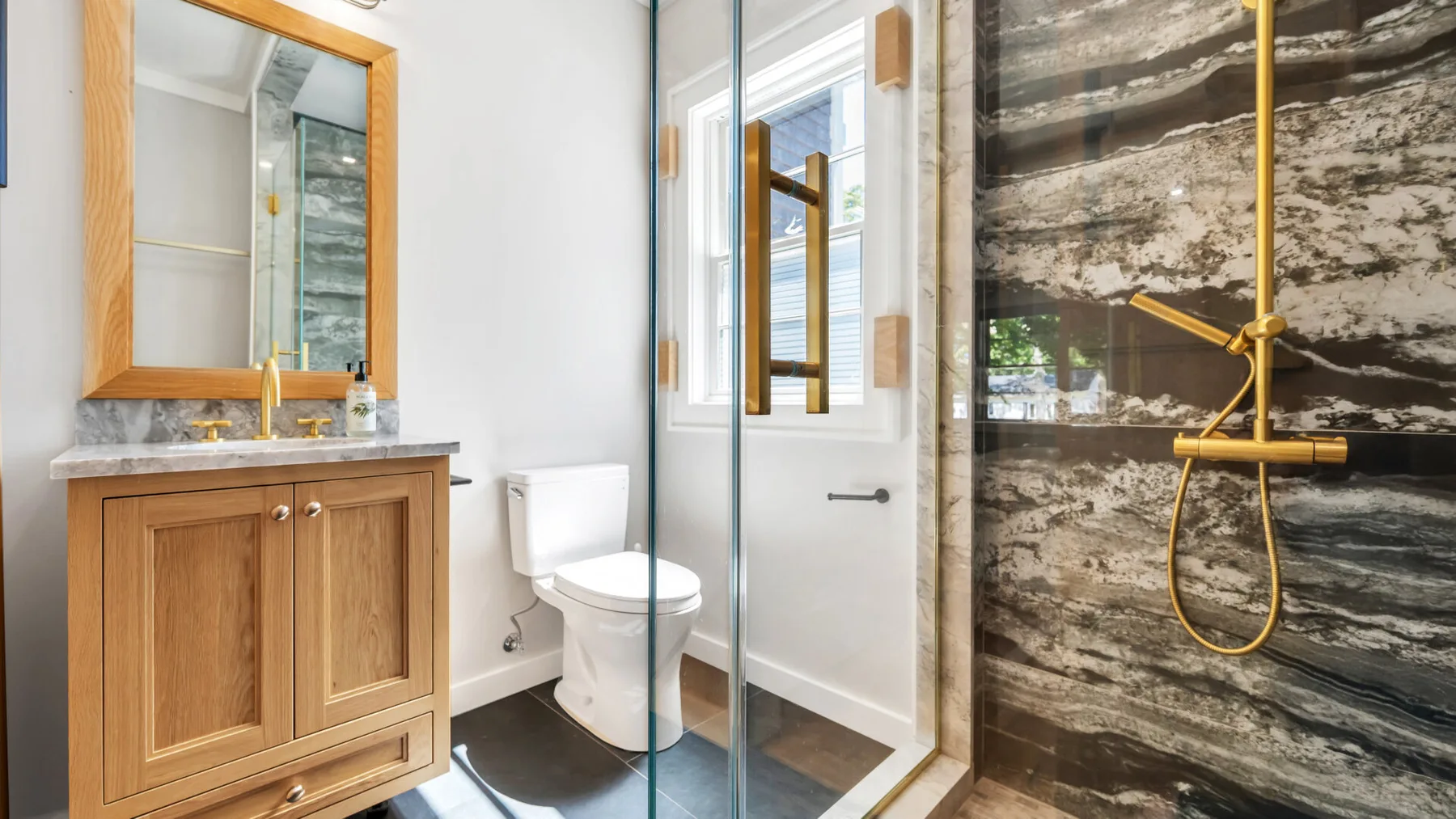 A bathroom with a glass shower, wooden vanity, and toilet.