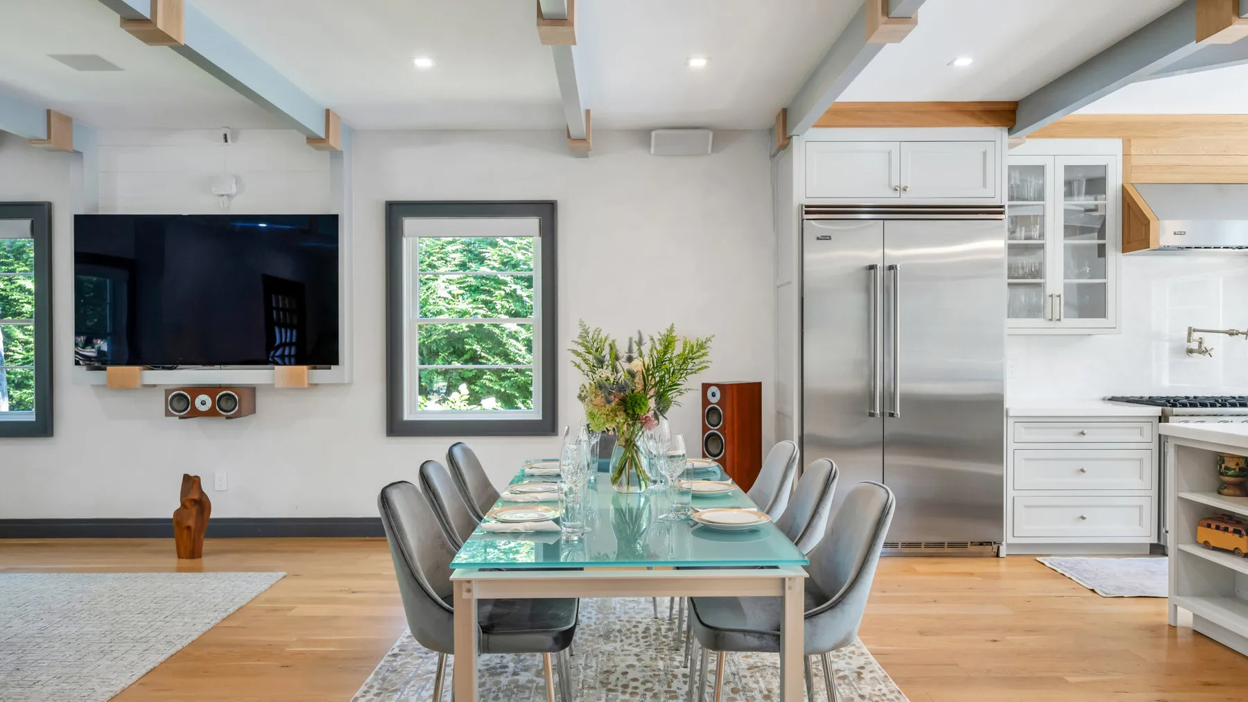 A dining area with a glass table and chairs sits beside a kitchen.