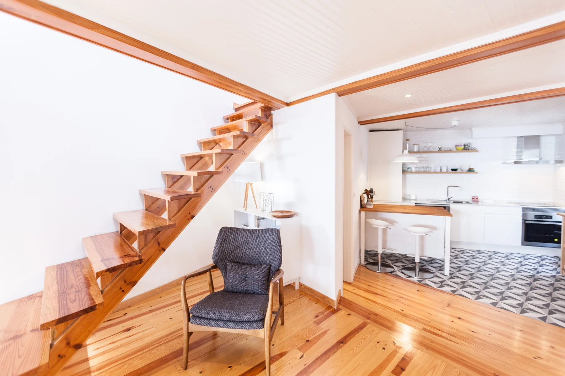 A living area with a wooden staircase opening onto a bright kitchen.