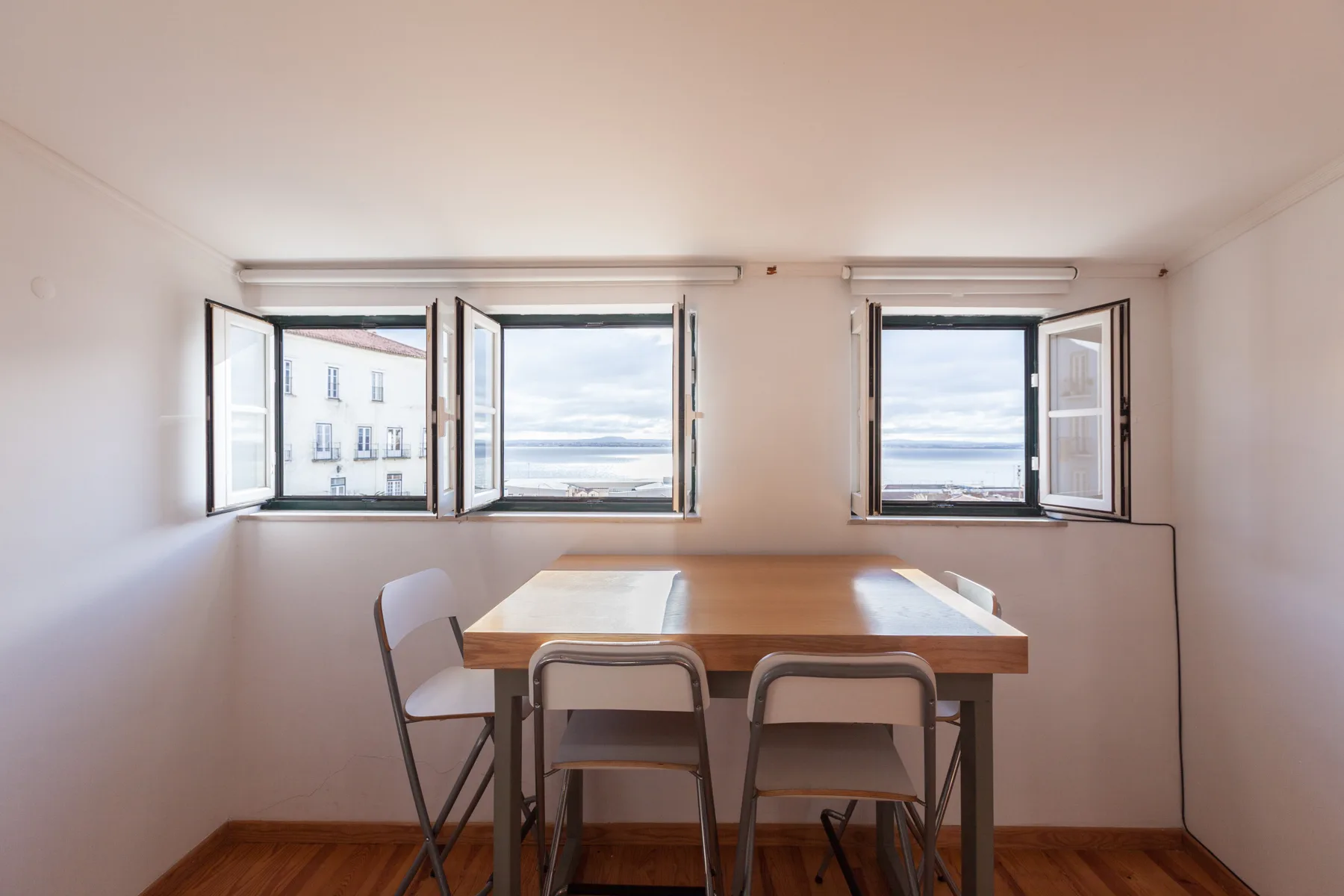 A dining area with a table and chairs beside open windows.