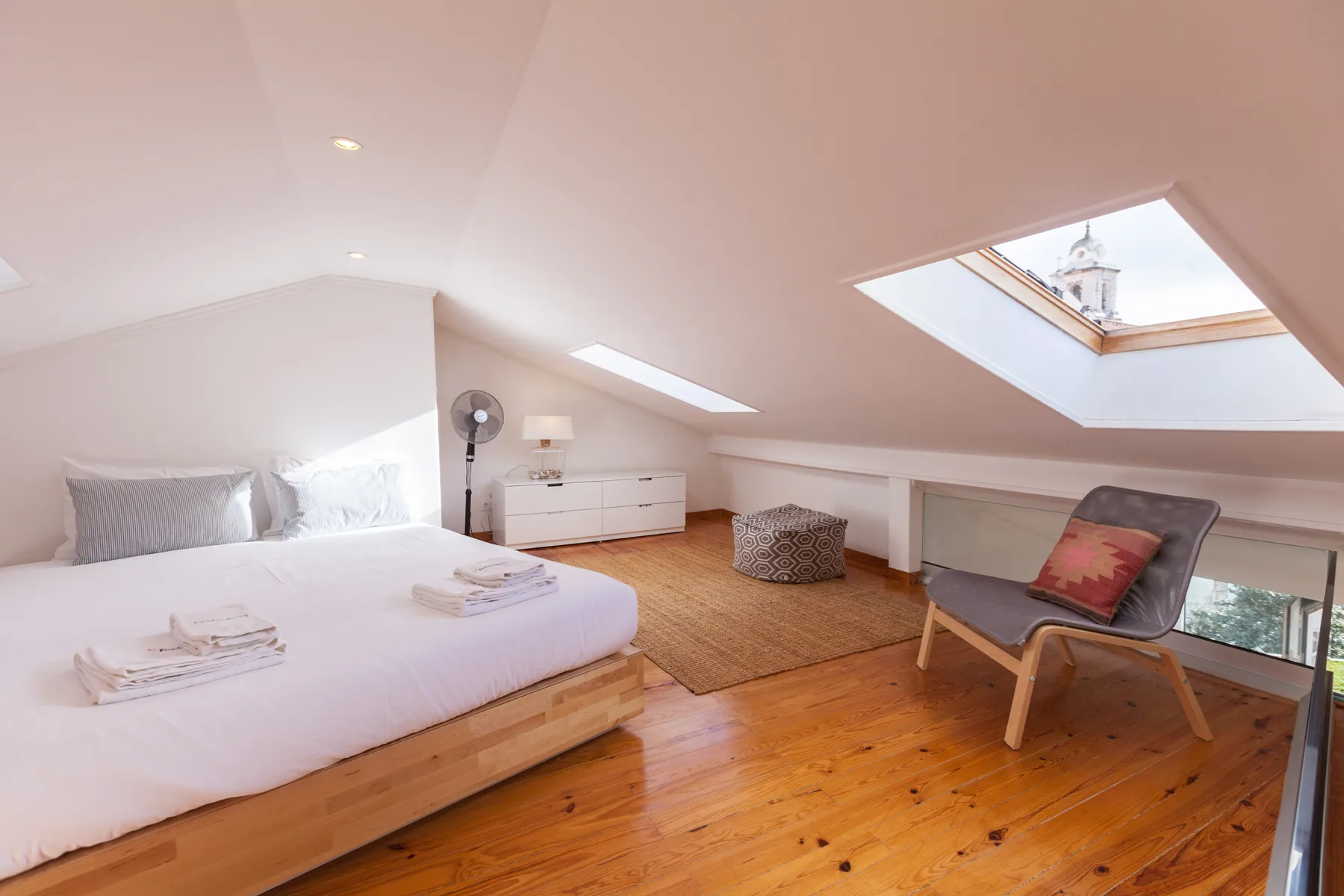 A bright attic bedroom has a low bed, a chair, and a skylight.