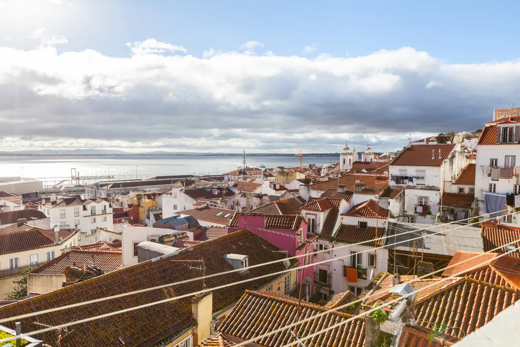 A cityscape of red-tiled rooftops overlooks the water beneath a cloudy sky.