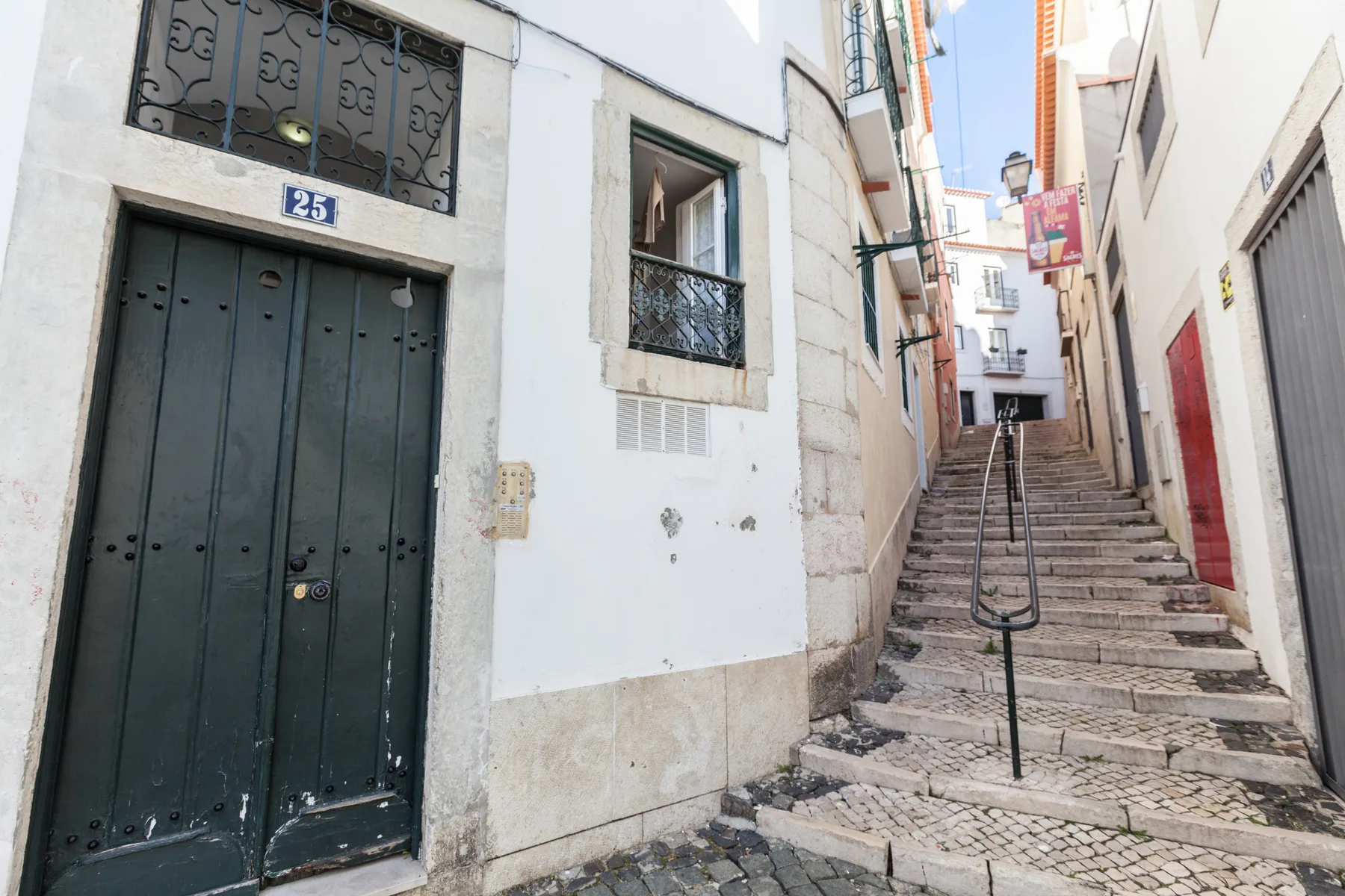 A narrow cobblestone street climbs between white buildings, with stairs and a handrail.