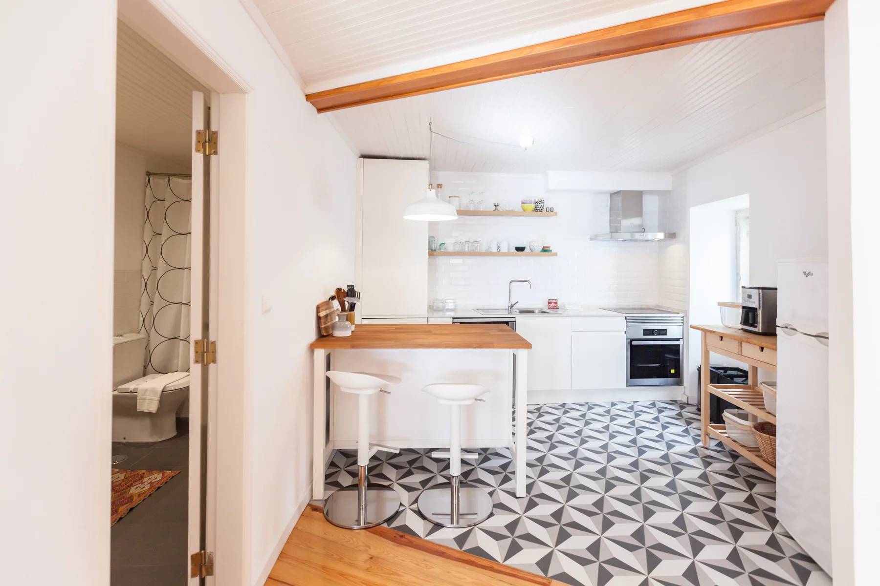 A bright kitchen with a breakfast bar, white cabinets, and patterned floor tiles.
