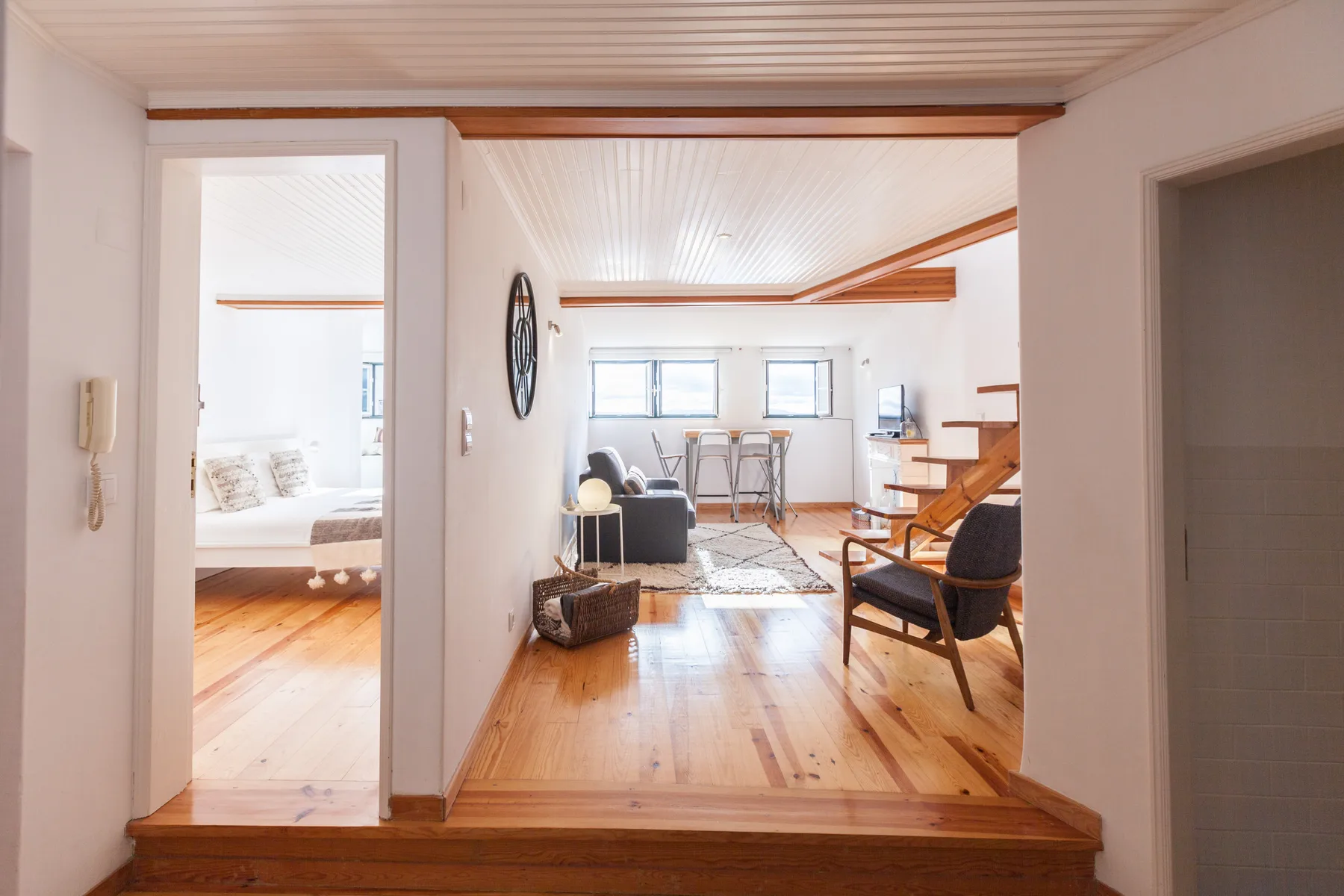 Interior luminoso de apartamento con zona de estar, mesa de comedor y escalera de madera.