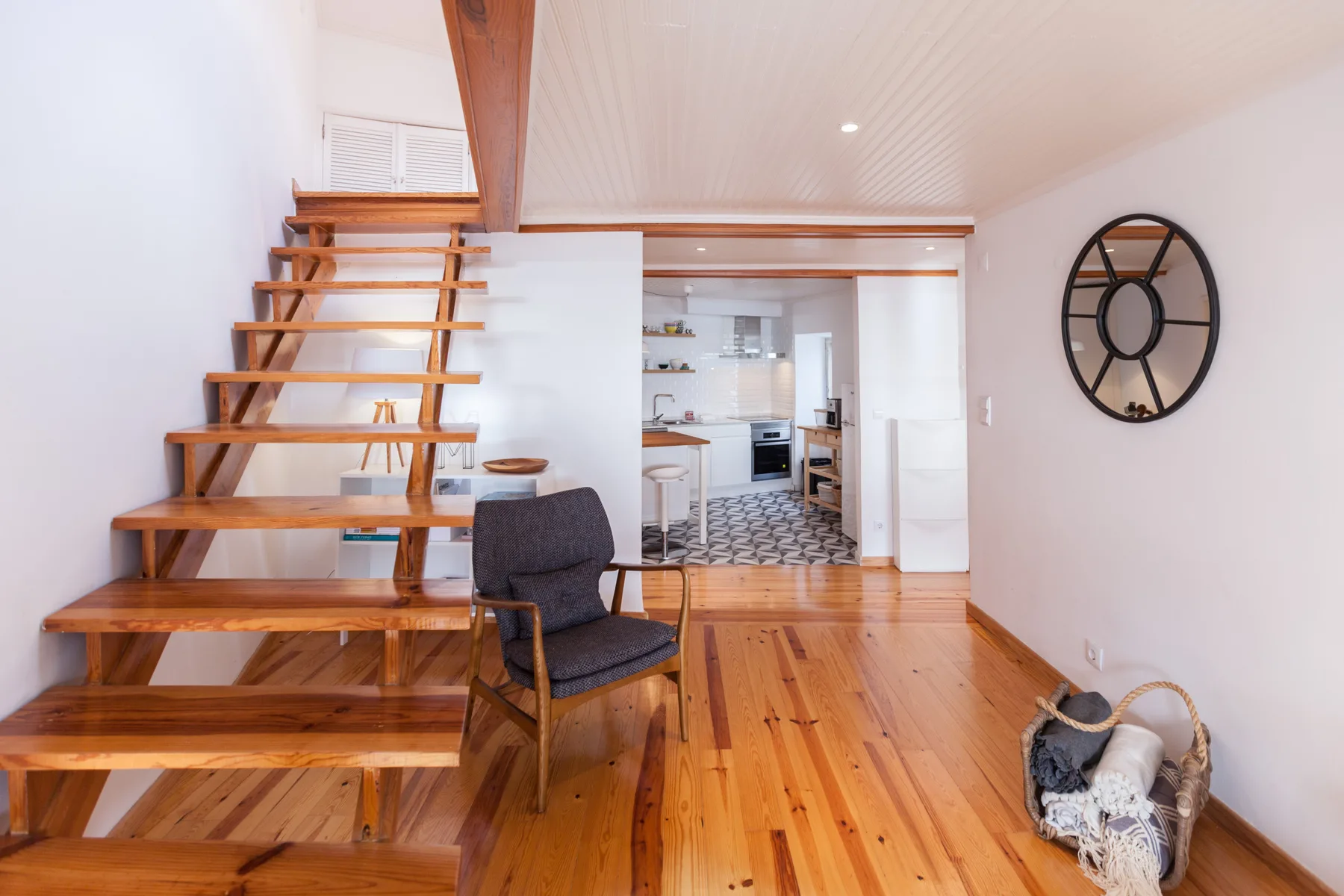 An open interior with a wooden staircase leading to an upper level and a kitchen beyond.