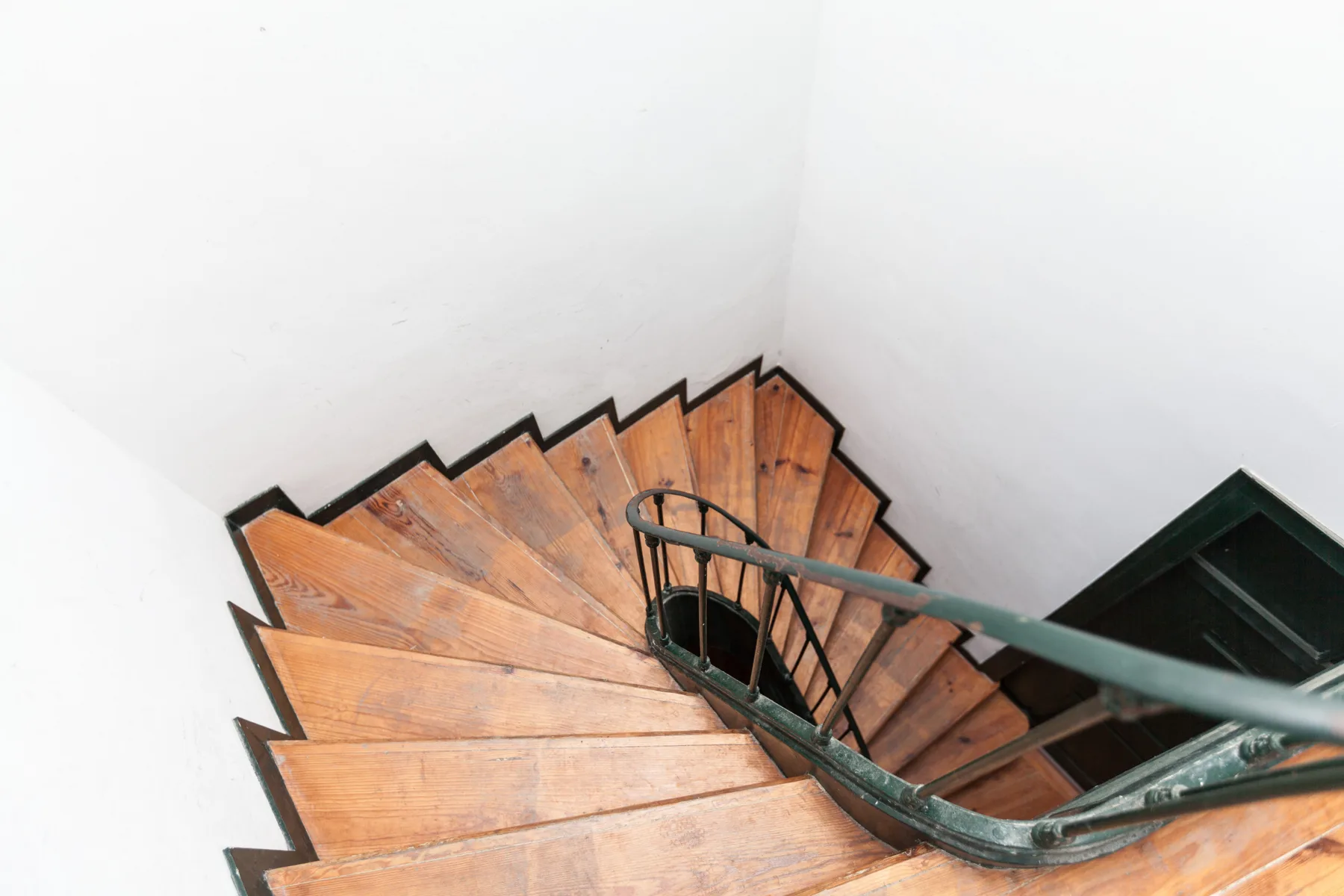 A curved wooden staircase with a dark metal railing descends through a white interior.