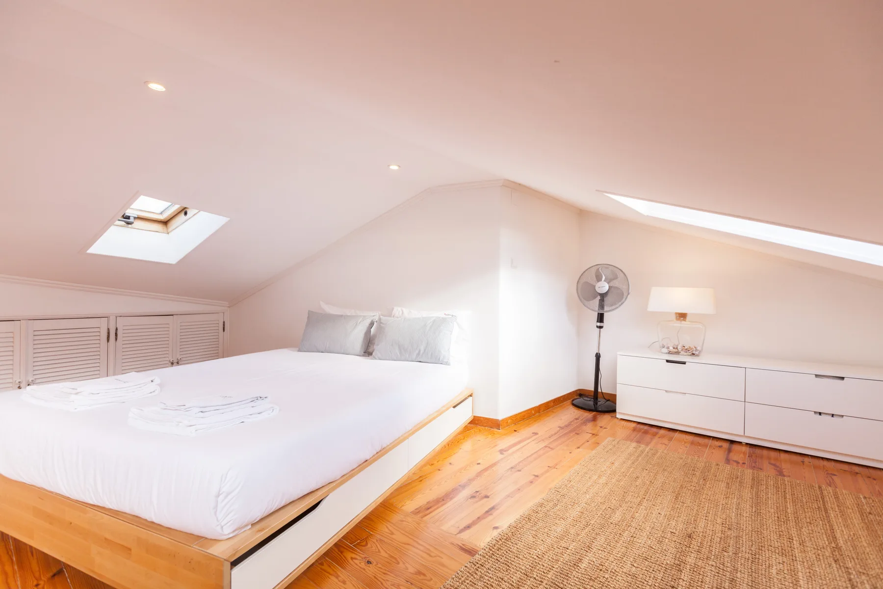 A bright attic bedroom with a large bed and sloped ceiling.