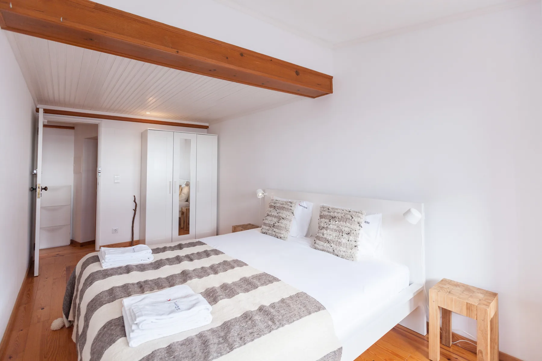 Un dormitorio con una cama, ropa de cama a rayas y un armario junto a la puerta abierta.