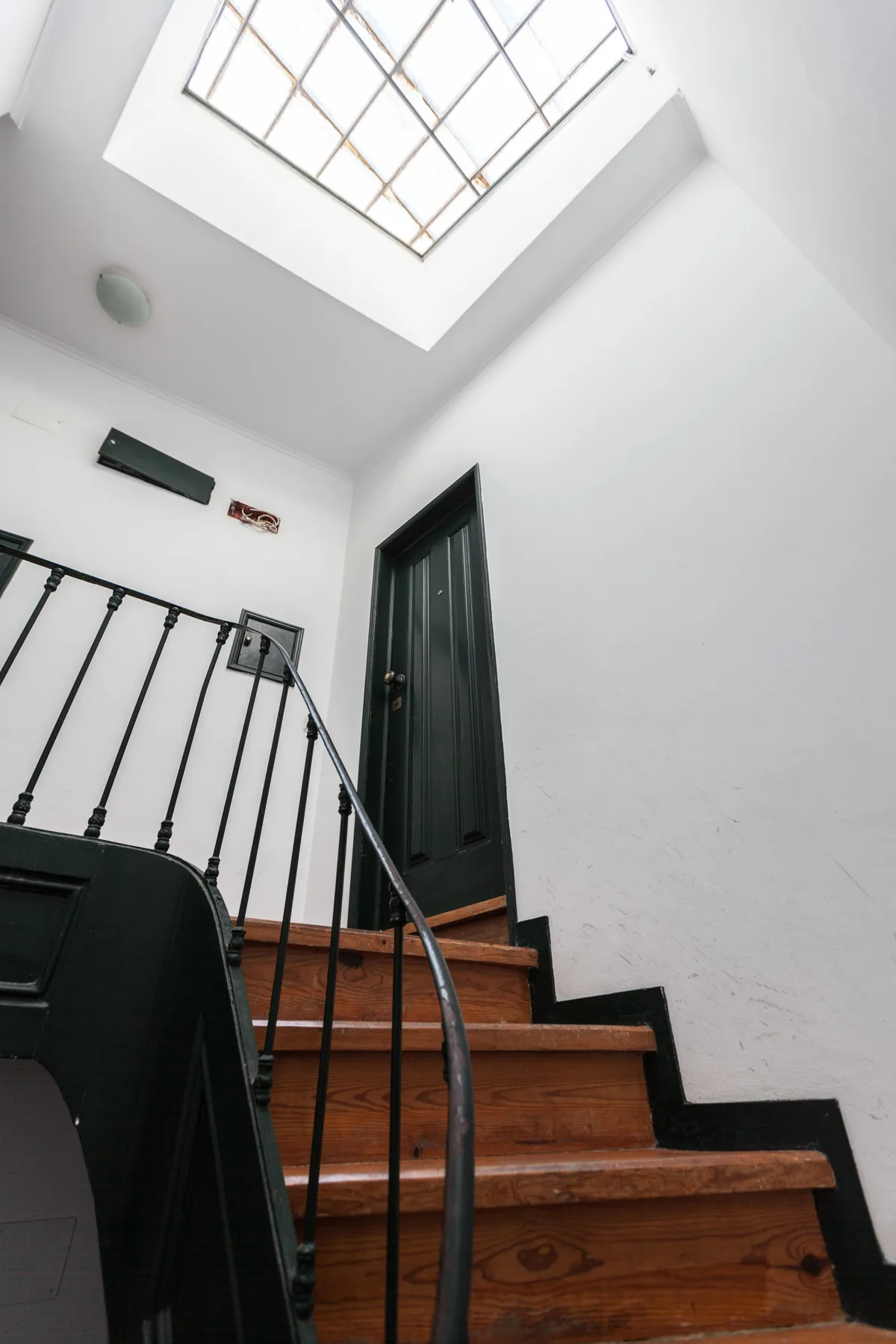 A staircase with wooden steps rises toward a dark doorway beneath a skylight.