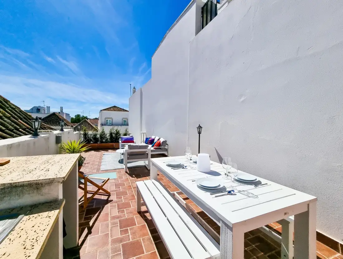 A sunny rooftop terrace with outdoor dining furniture and seating.