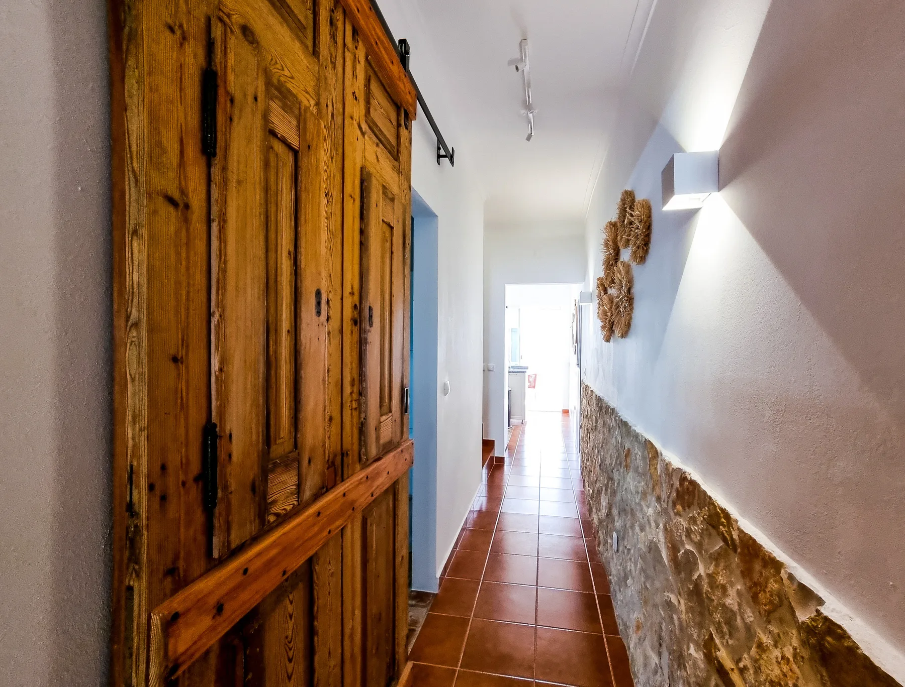 A narrow hallway with terracotta floor tiles and a wooden door.