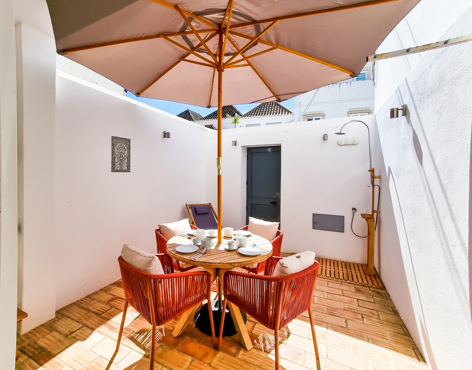 A tiled outdoor terrace has a round dining table beneath a large umbrella.