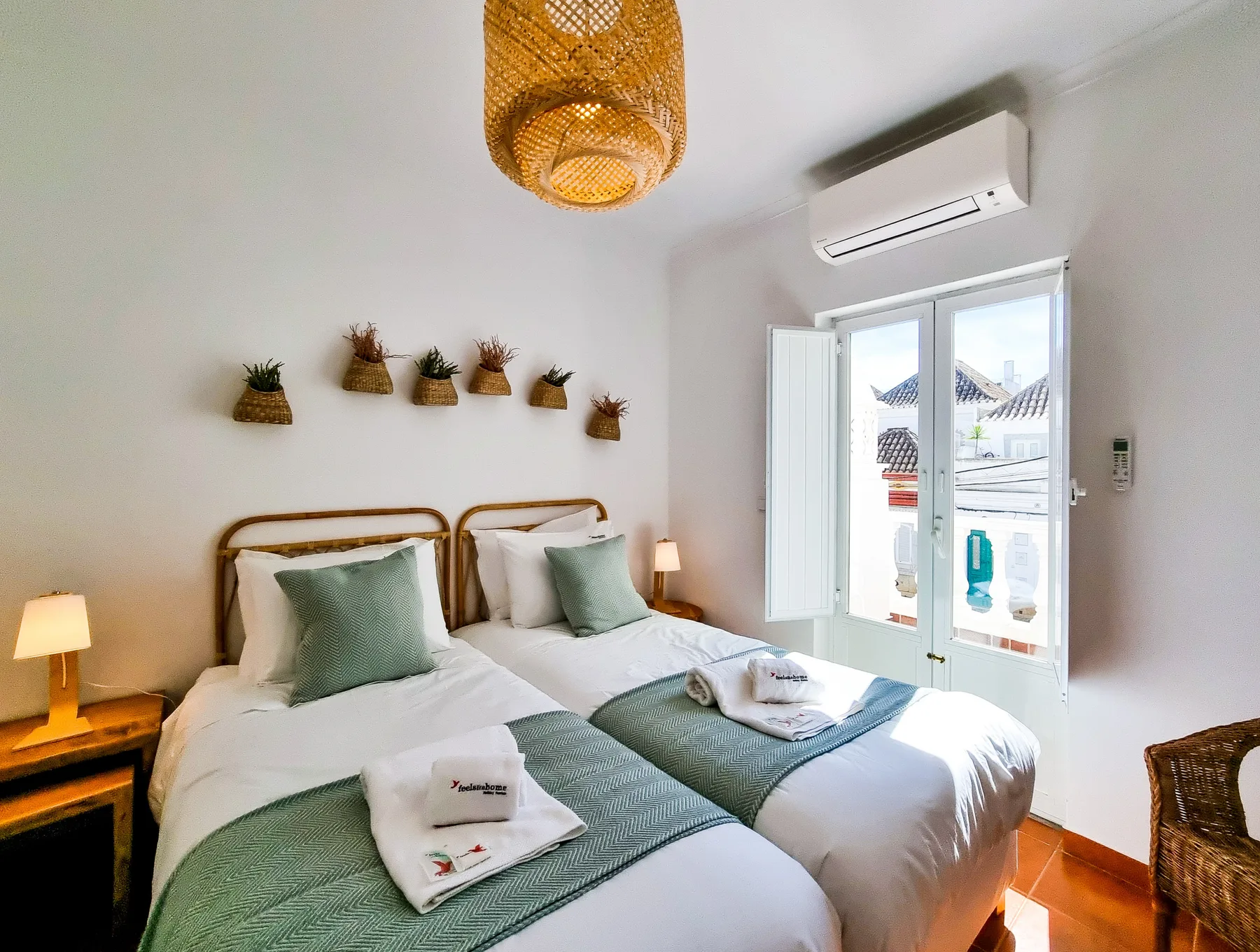 A bright bedroom with twin beds, green bedding, and a window.