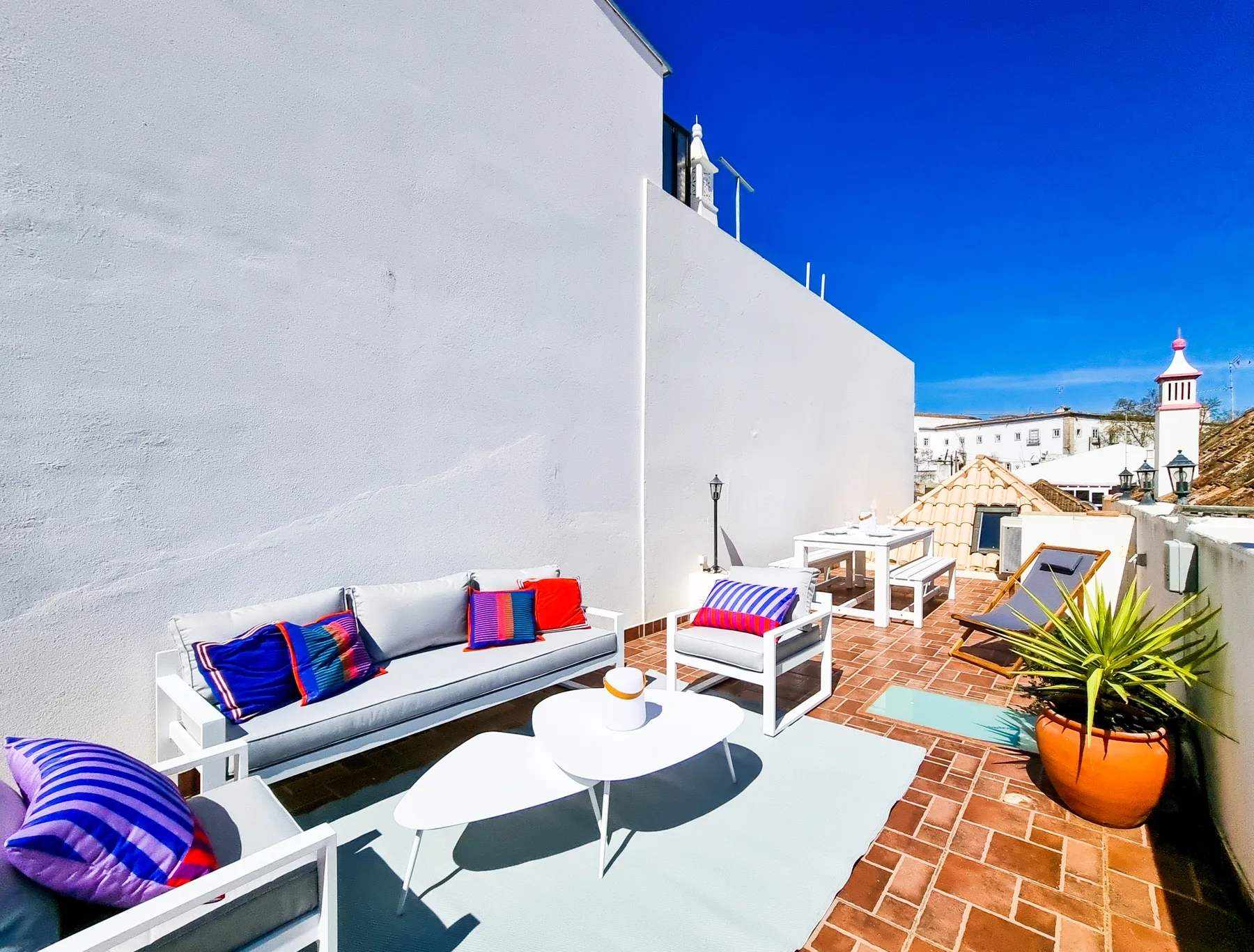 A rooftop terrace with outdoor seating, potted plants, and views of nearby buildings.
