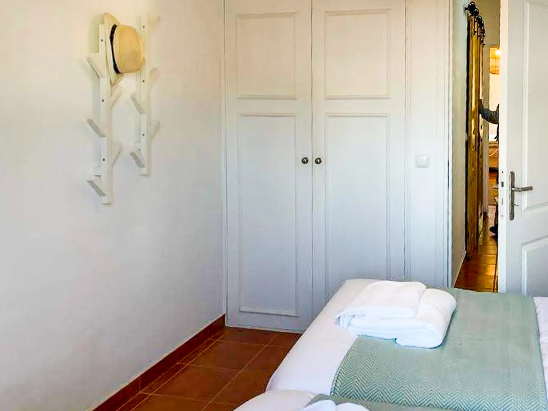 A bedroom with a bed, folded towels, and a wall-mounted coat rack.