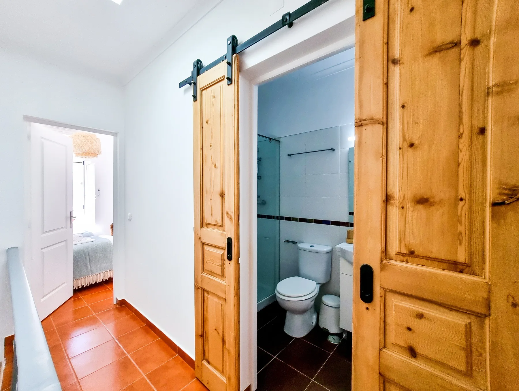 A white hallway with wooden sliding doors opens onto a bathroom and bedroom.