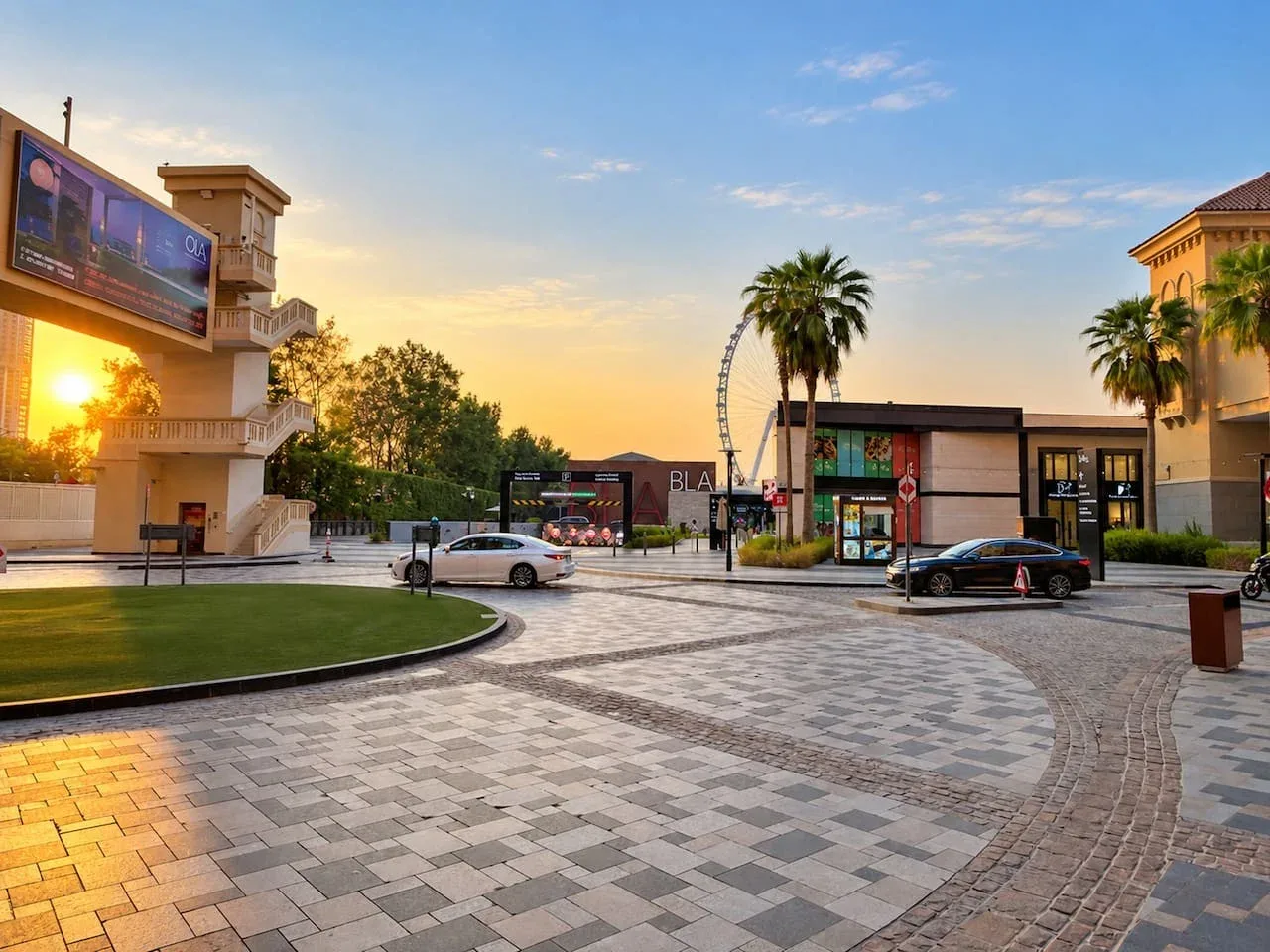 An outdoor shopping plaza with storefronts and palm trees at sunset.