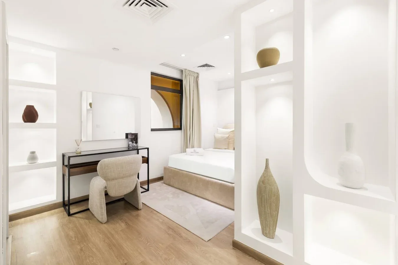 A bright bedroom with a desk beside the bed and decorative display shelves.