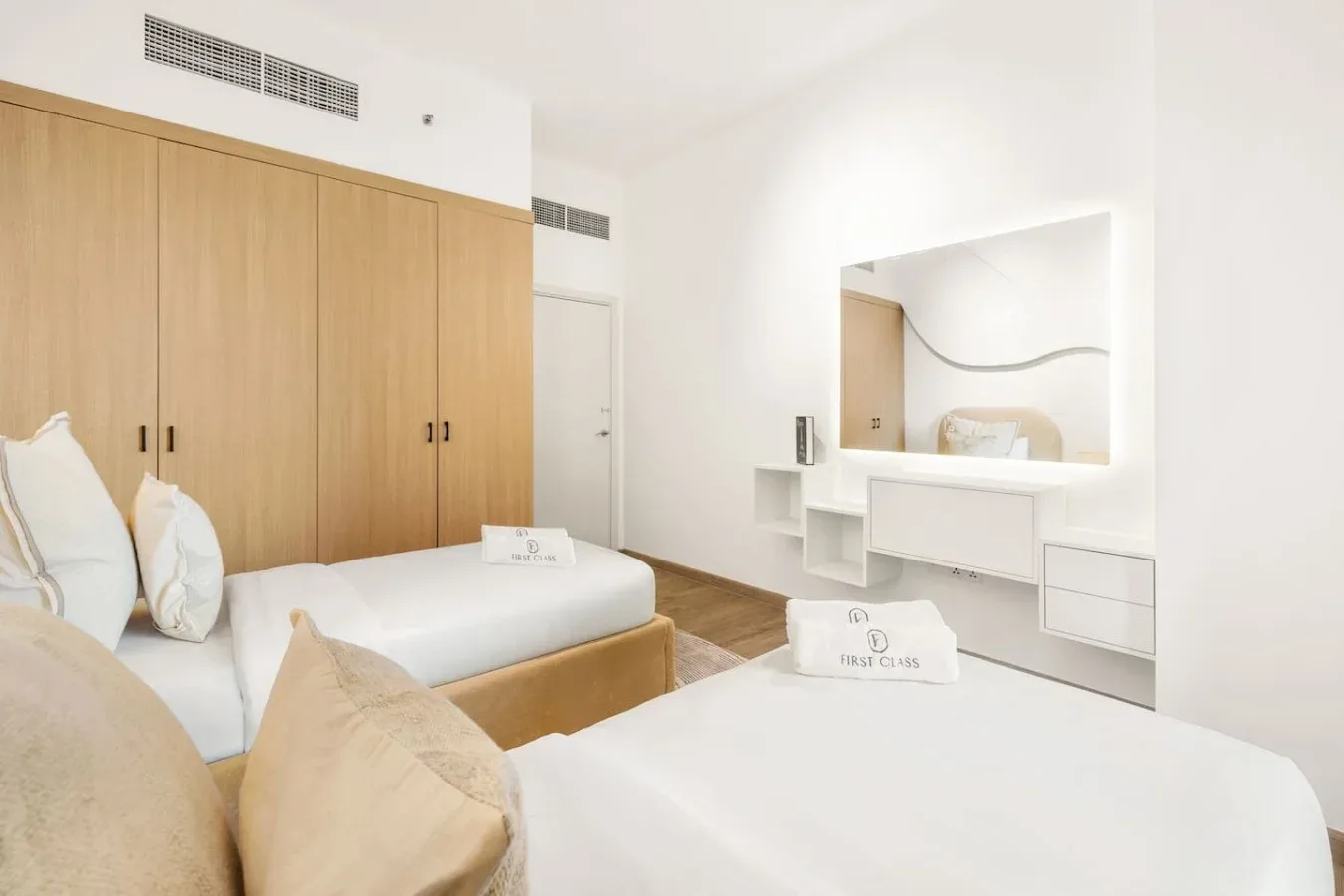 A bright bedroom with two beds and built-in wooden wardrobes.