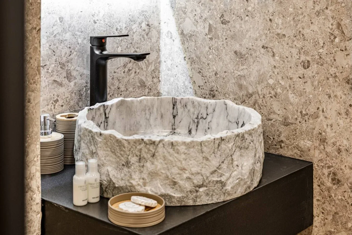 A stone vessel sink sits on a dark vanity beneath a black faucet.