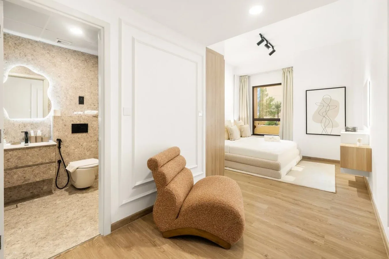 A bright bedroom with a bed, lounge seating, and an adjoining bathroom.