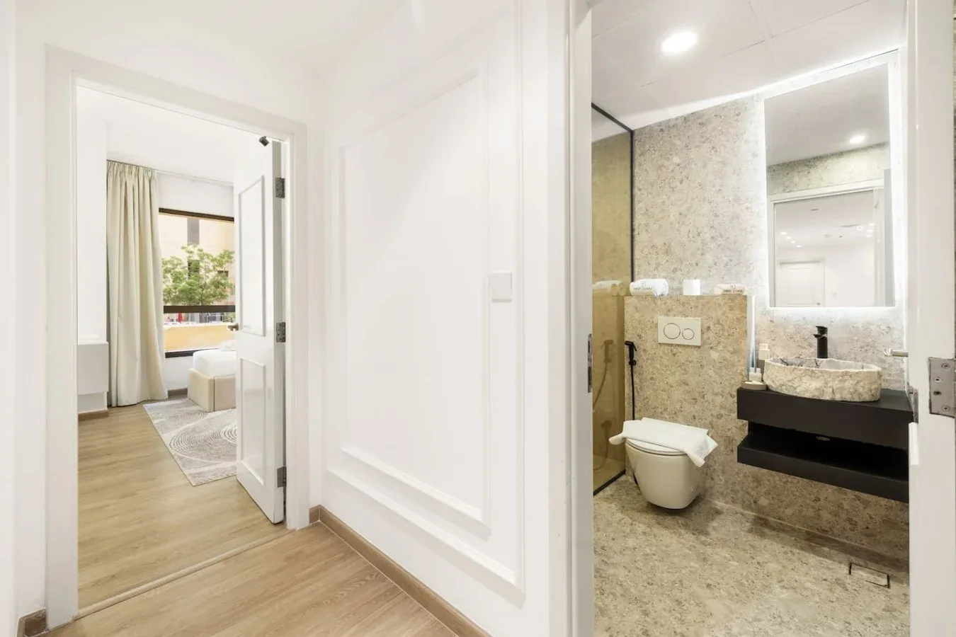 A bright hallway opens onto a bathroom with a toilet and sink.