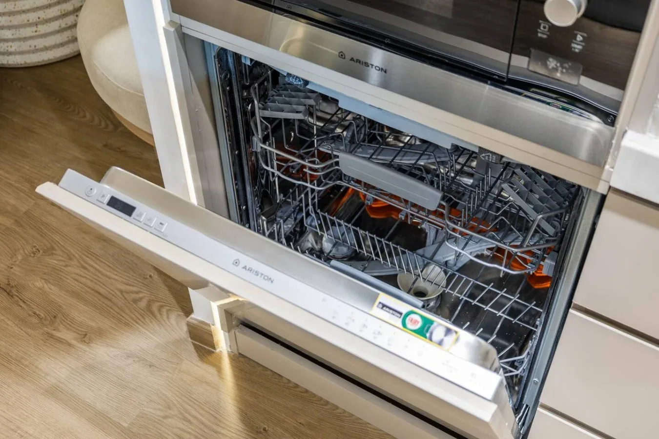 An open dishwasher with dishes and utensils inside, set into a kitchen cabinet.
