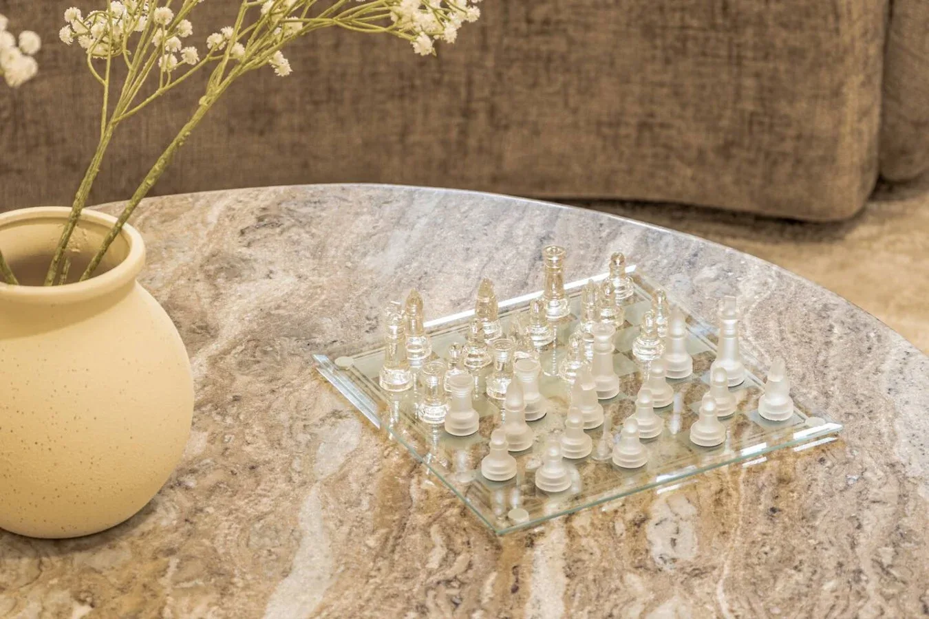 A chessboard sits on a stone coffee table beside a vase of flowers.