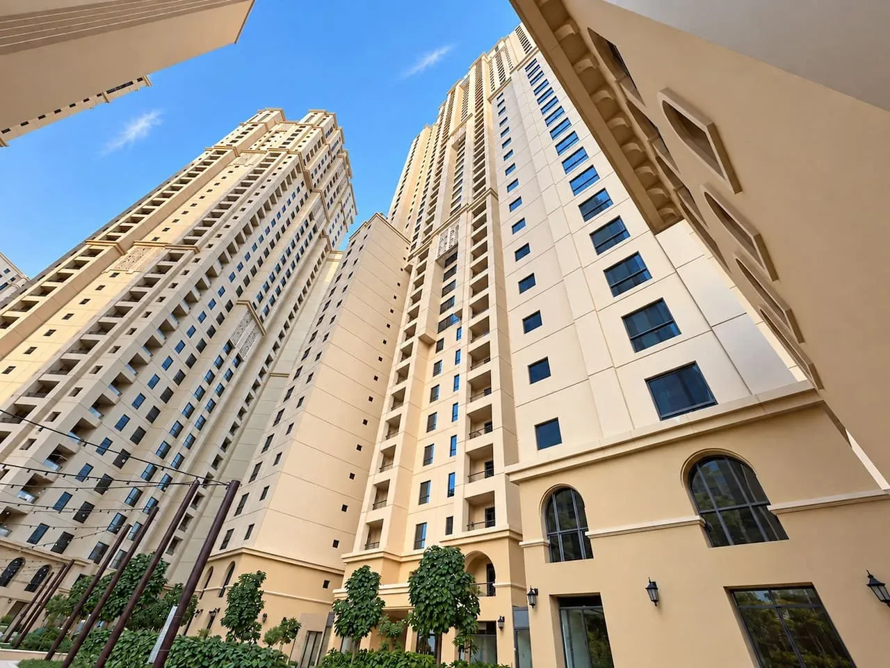 Tall beige apartment buildings rise around a landscaped courtyard beneath a clear blue sky.