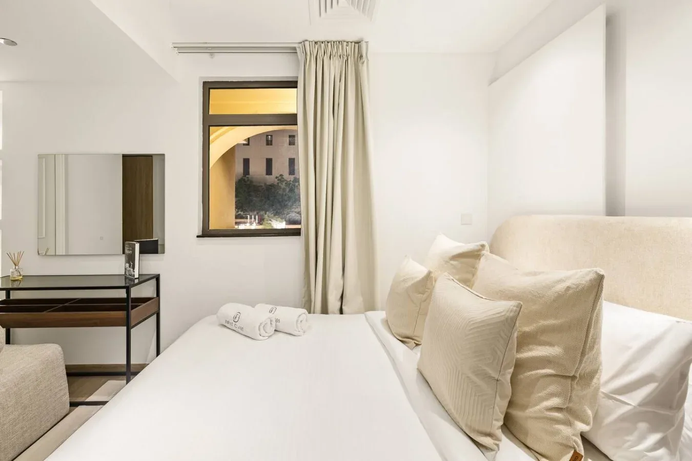 A bright bedroom with a bed beside a window and a small dressing table.