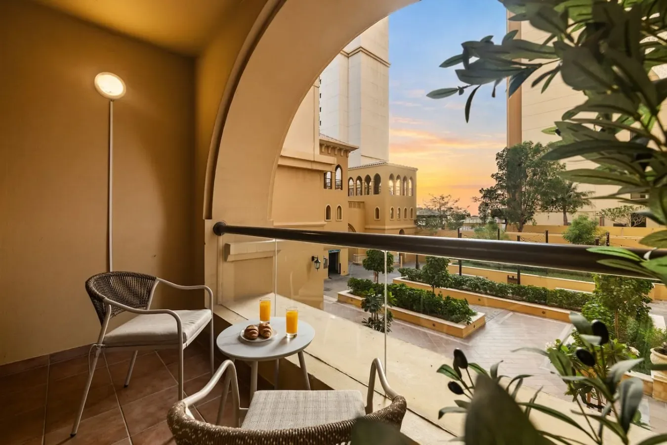 A balcony seating area overlooks landscaped grounds and buildings at sunset.