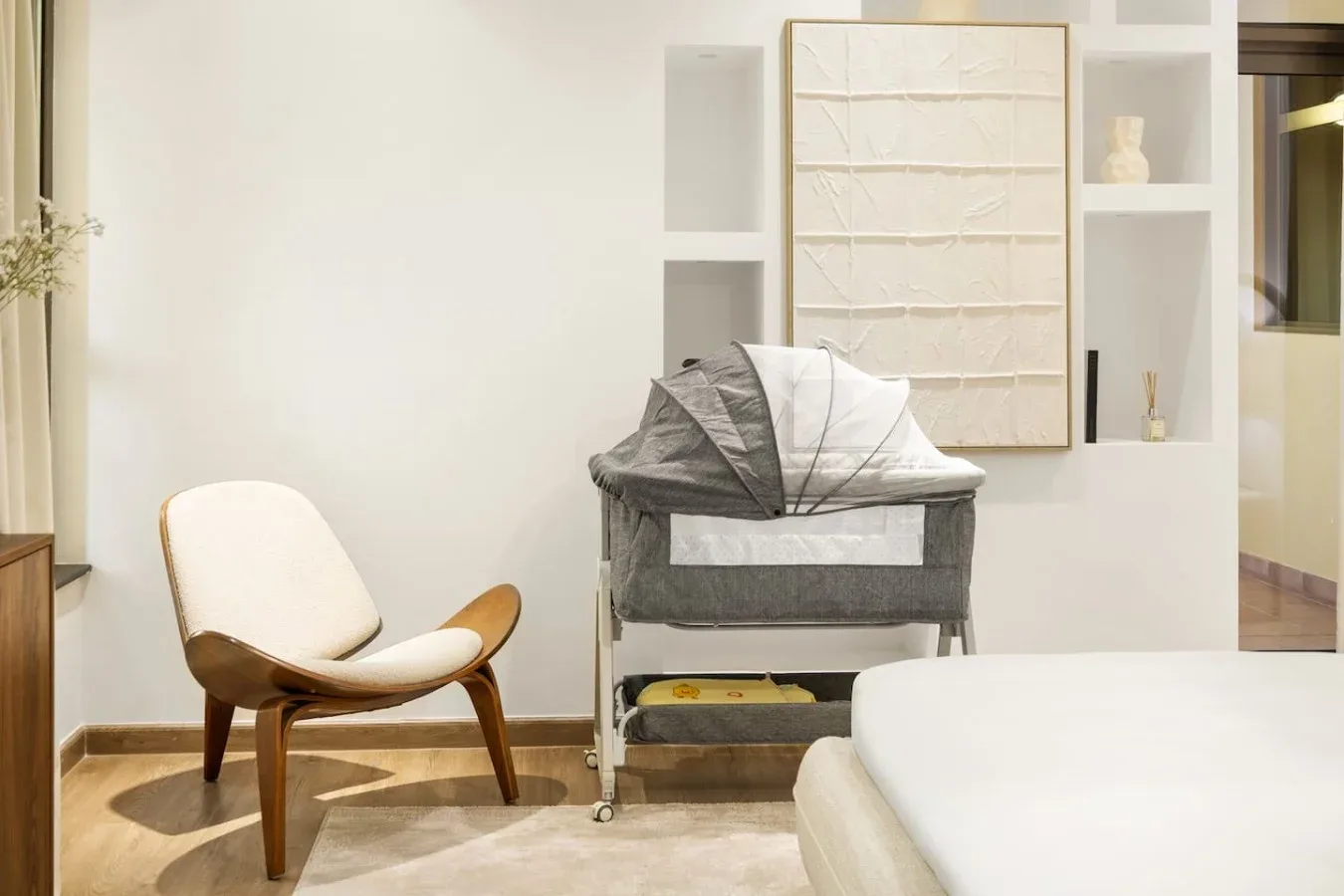 A bright bedroom with a bed and a chair beside a baby bassinet.