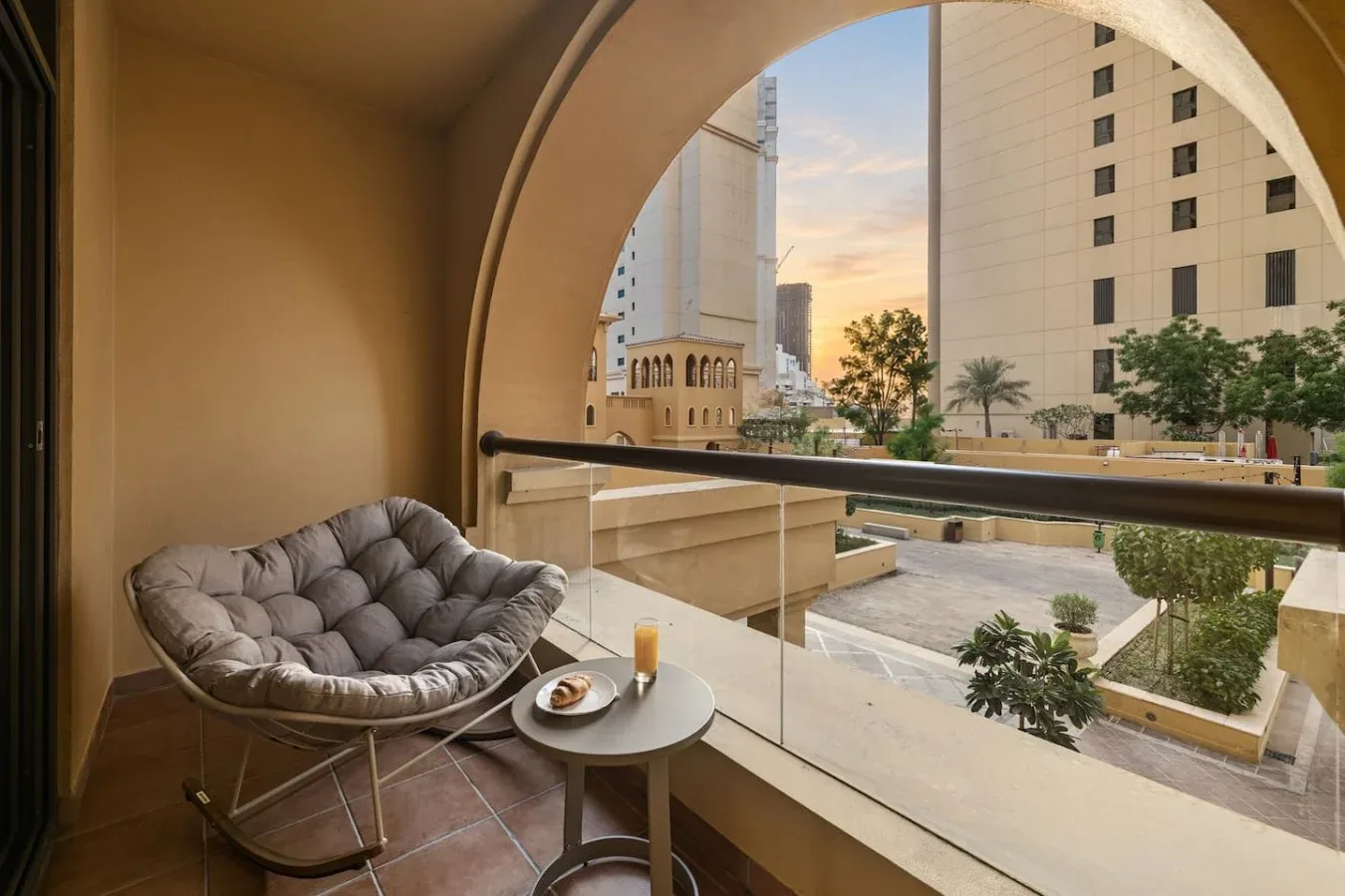 A balcony seating area overlooks nearby buildings through a large arched opening.