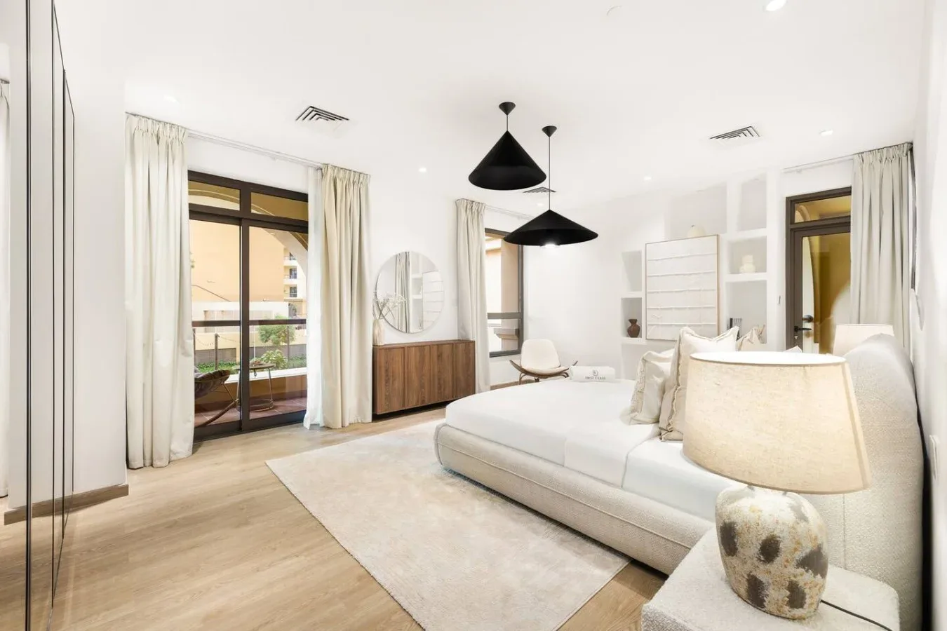 A bright bedroom with a large bed, pendant lights, and curtained glass doors.