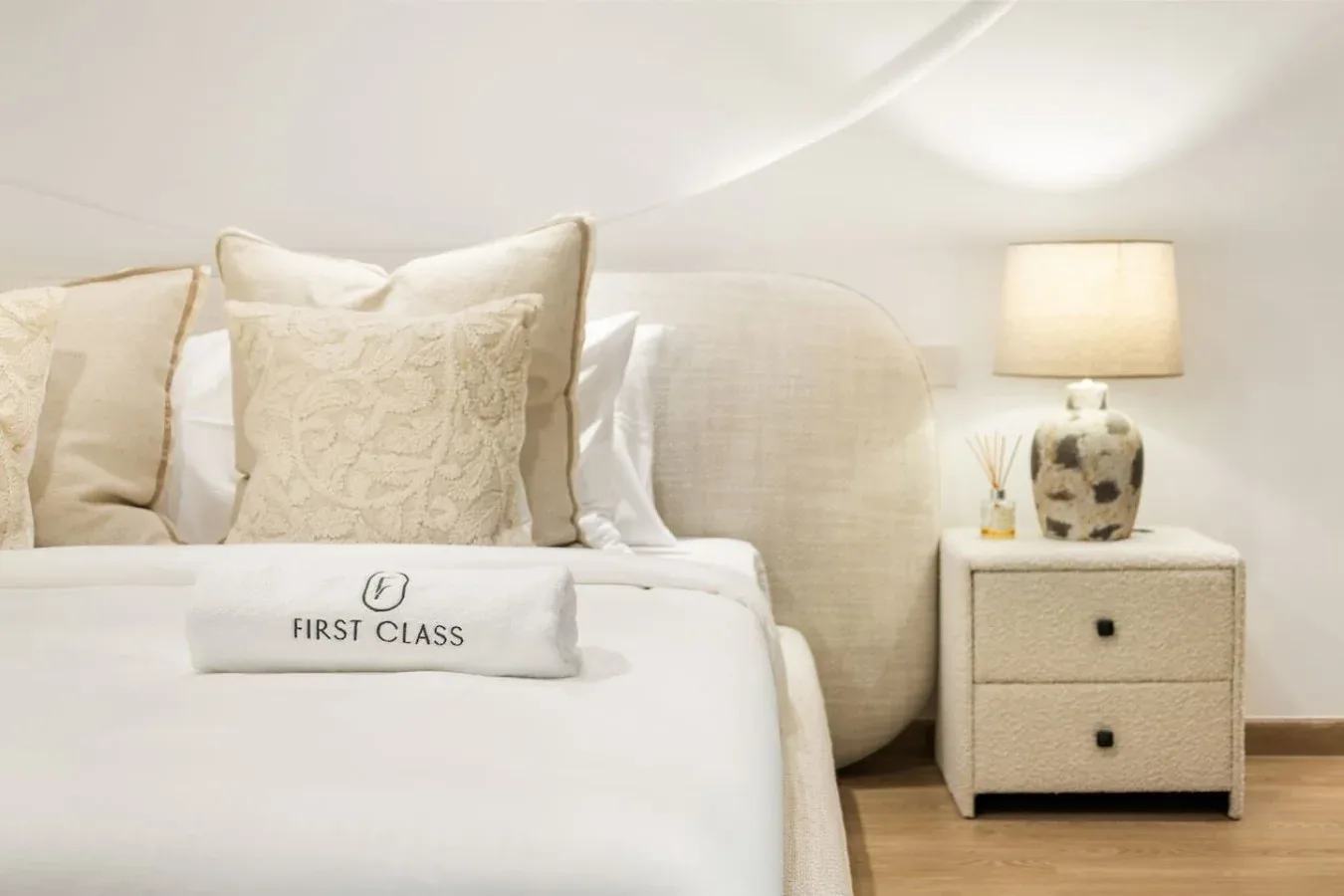 A neatly made bed with decorative pillows sits beside a lit bedside lamp.