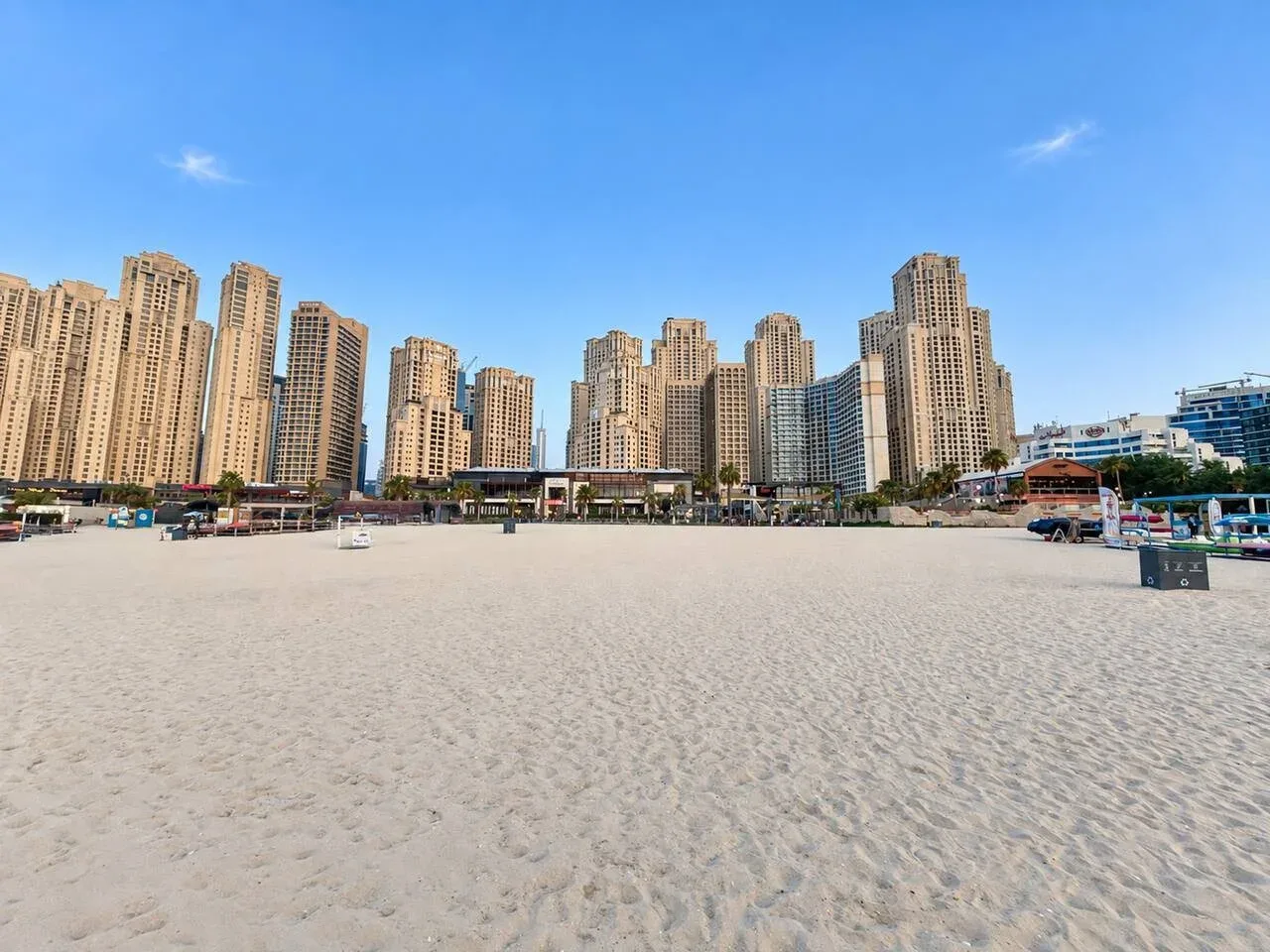 A broad sandy beach stretches toward a skyline of tall city buildings.