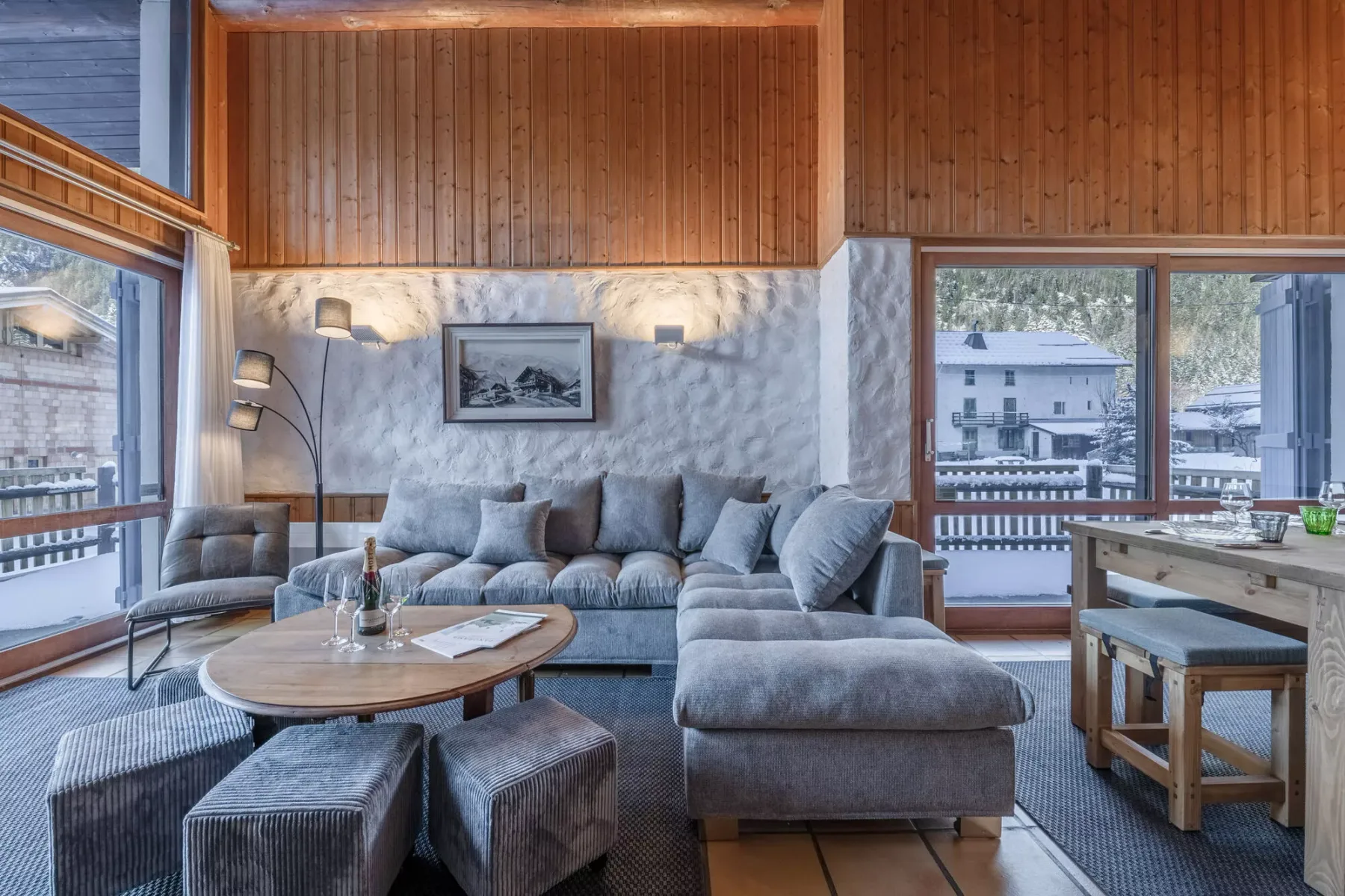 Una sala de estar con asientos alrededor de una mesa baja y ventanas grandes.