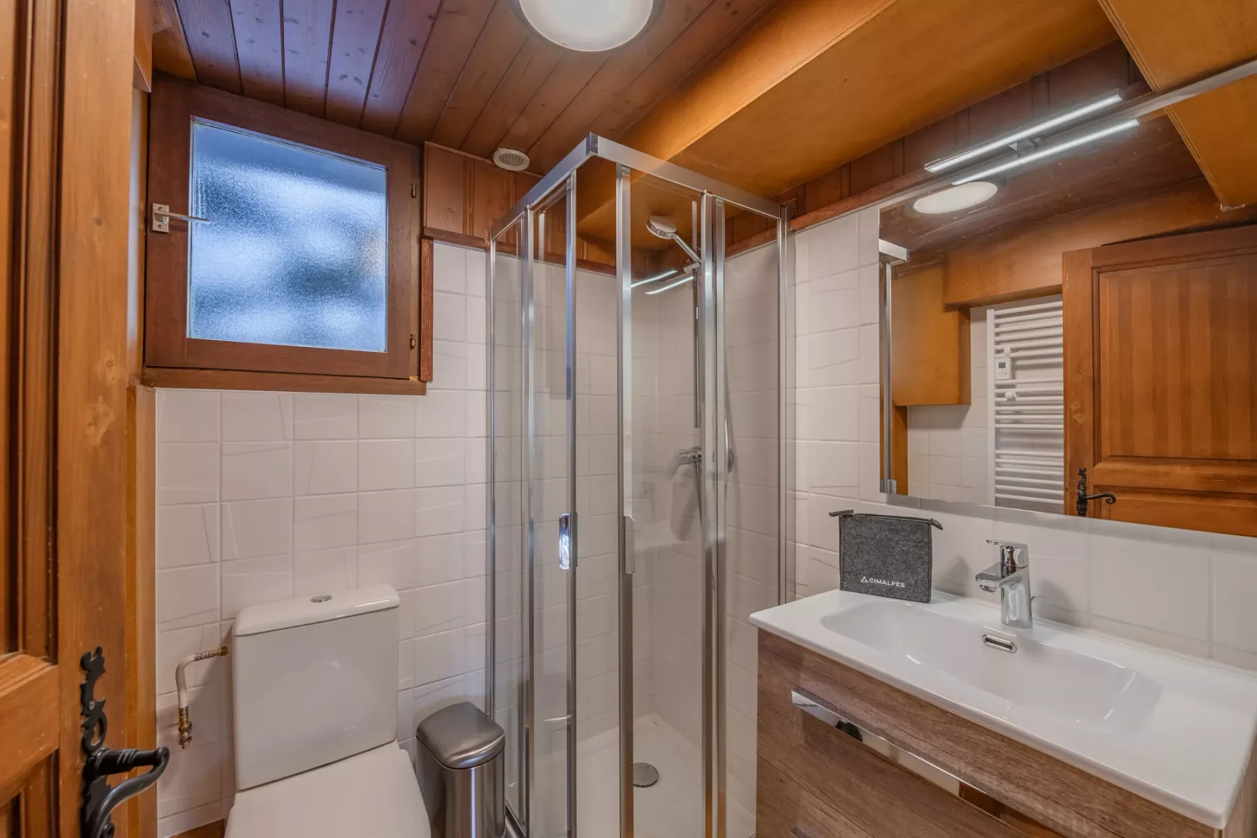 Un baño con ducha de vidrio, lavabo y techo revestido de madera.