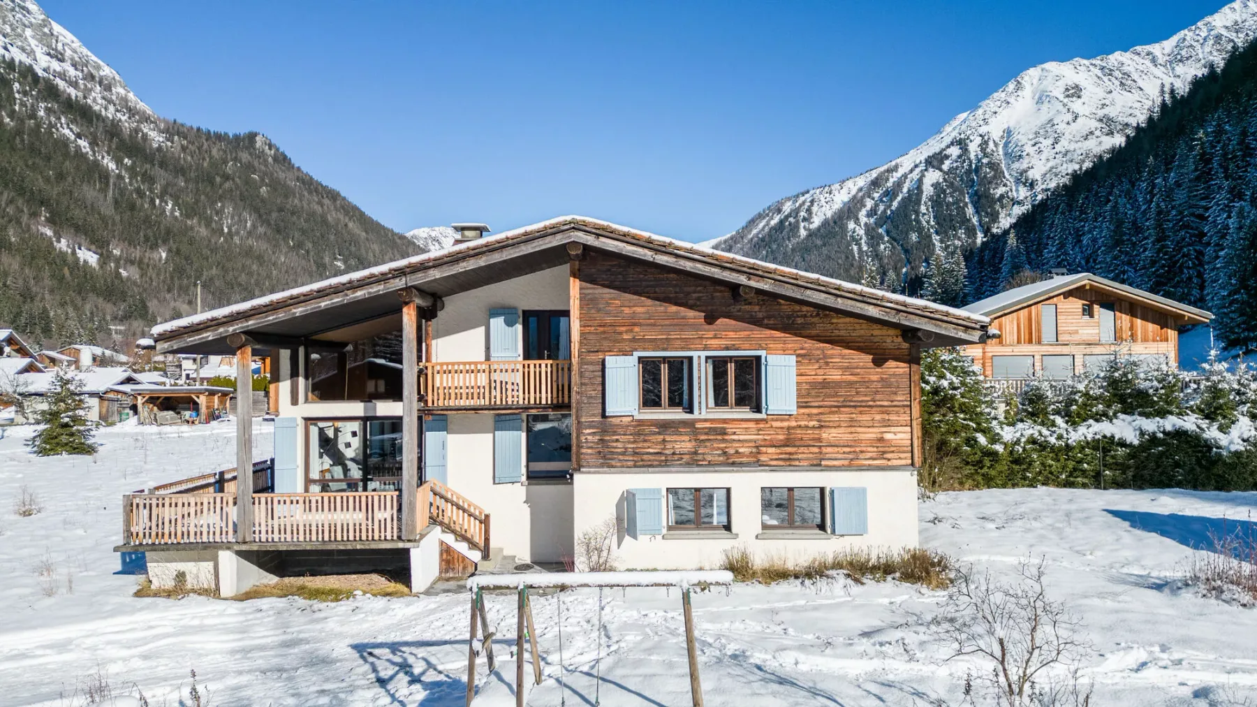 Un chalet de madera se alza en un paisaje montañoso nevado bajo un cielo azul despejado.