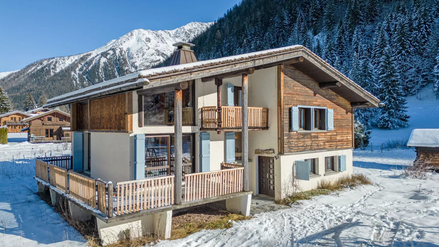 Un chalet está en un entorno montañoso nevado, con una veranda de madera.