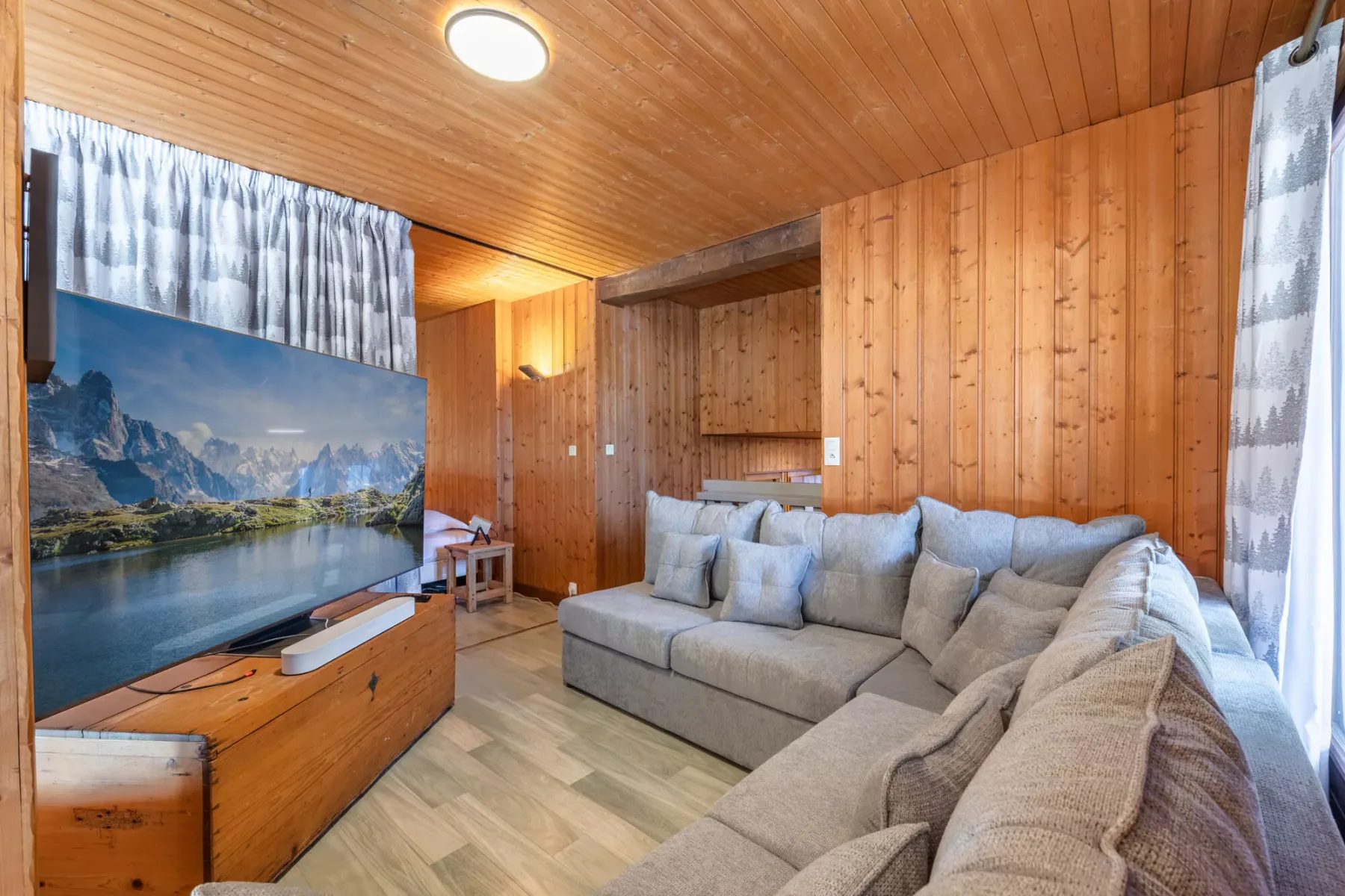 Una sala de estar con asientos grises, paredes de madera y una gran pantalla con un paisaje.