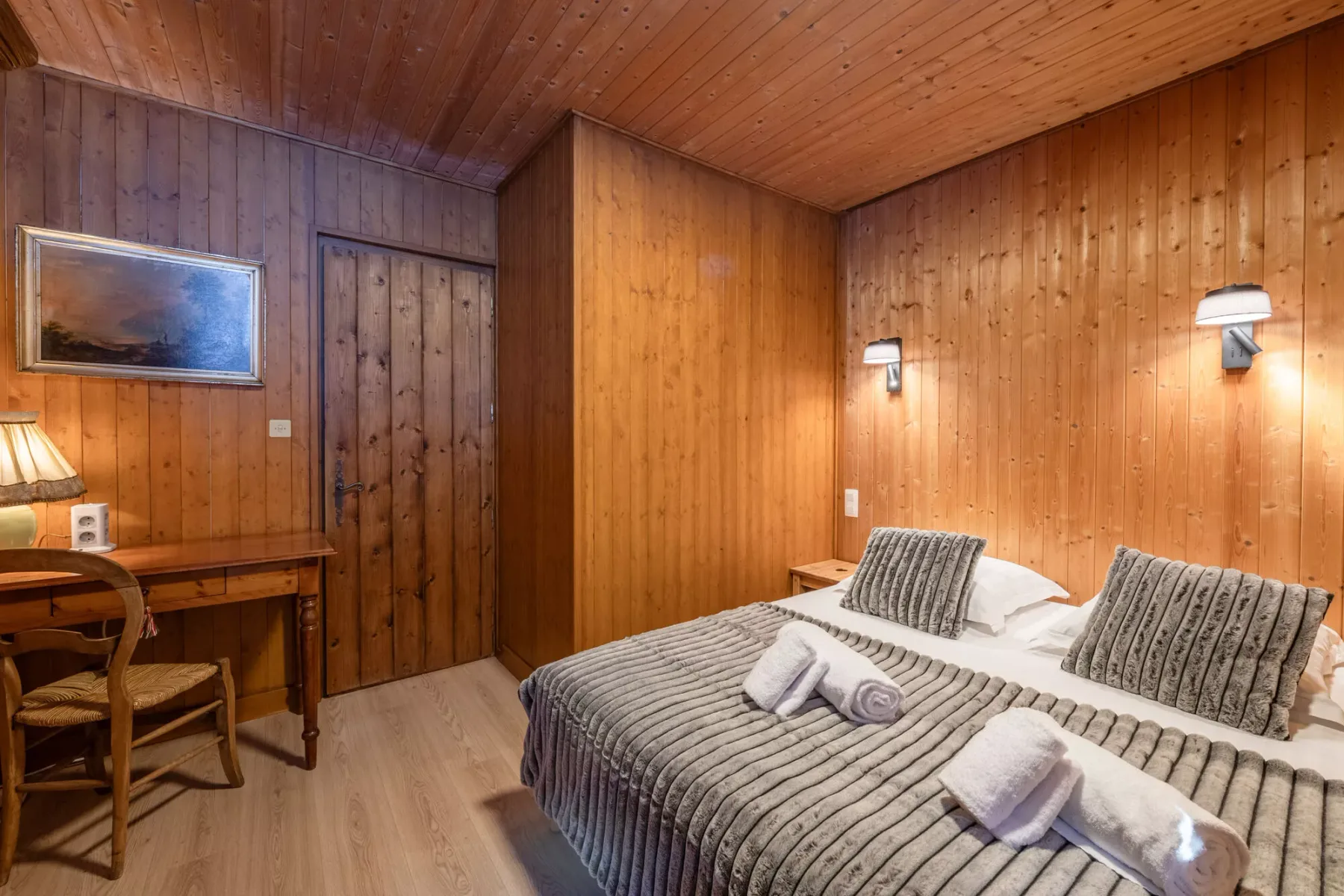 Dormitorio revestido de madera con camas individuales y toallas dobladas.