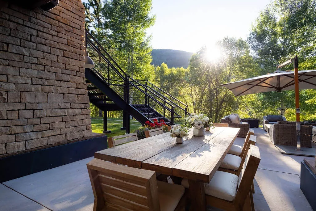 An outdoor dining area with a wooden table, seating, and a large umbrella.