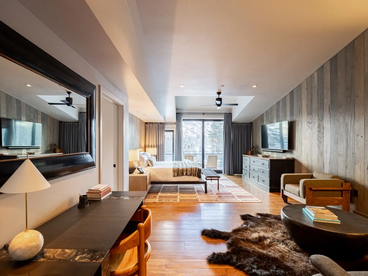 A bedroom and sitting area with a bed, television, and large windows.