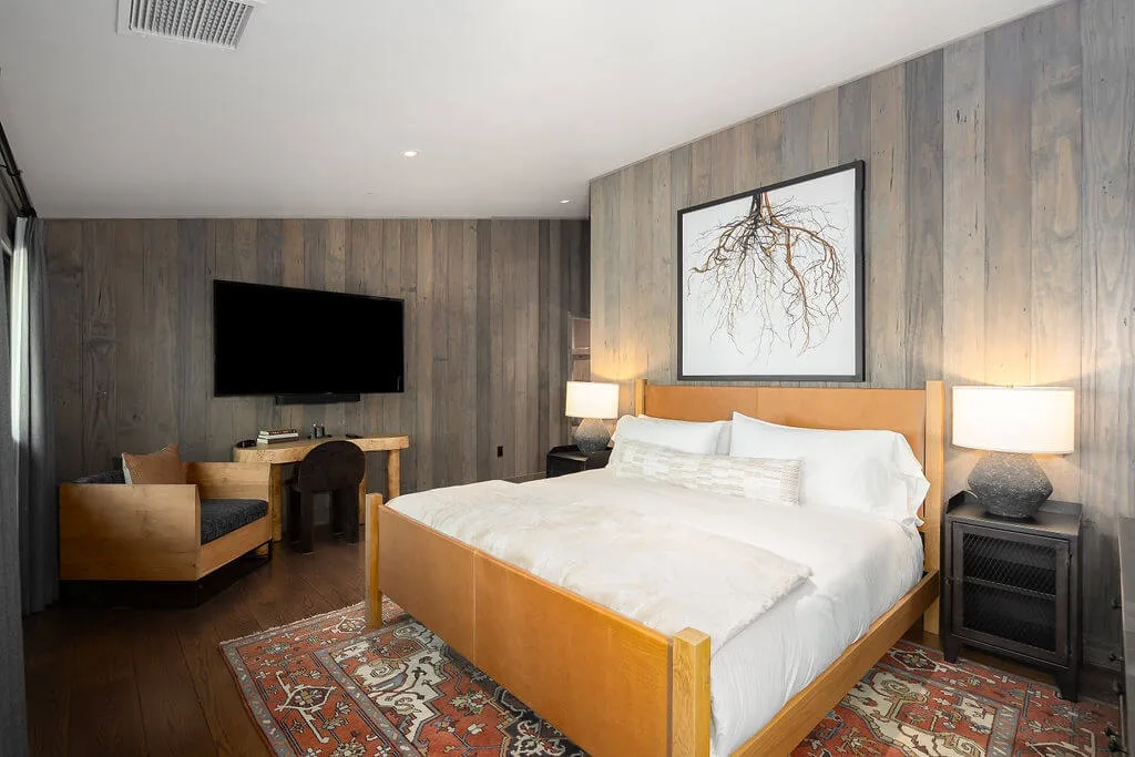 A bedroom with a large bed, framed artwork, and a television on the wall.
