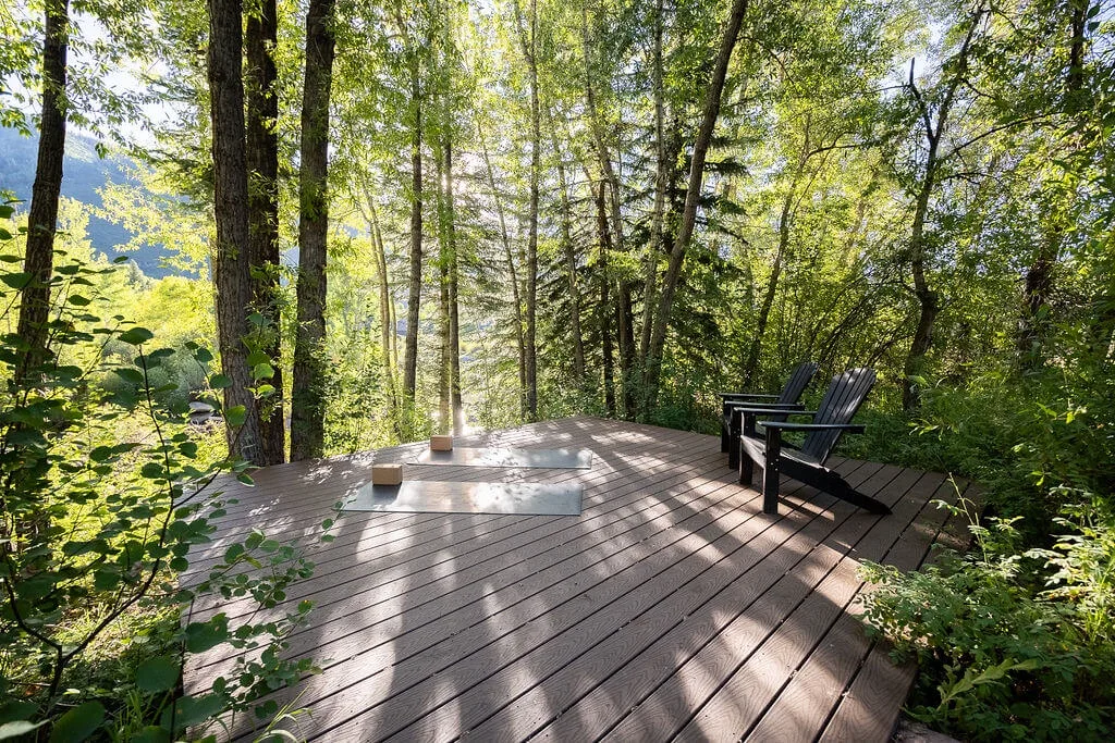 A wooden deck sits among trees, with outdoor seating and a small table.
