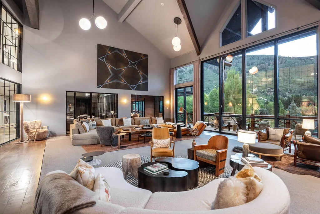 A spacious living room with seating arranged around low tables and large windows.
